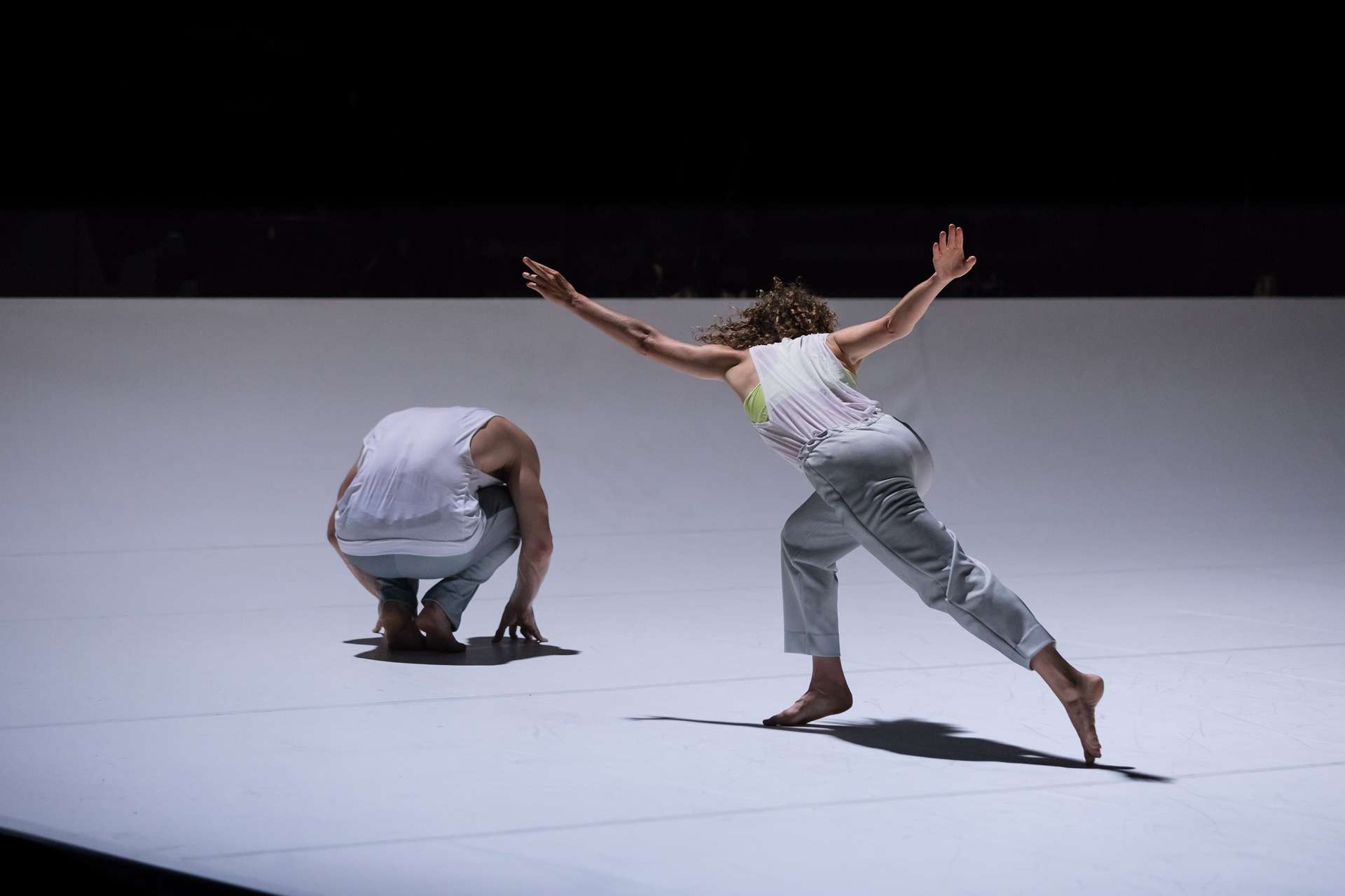 Deux interprètes, l'un de dos et accroupi et l'autre de dos en posture dansée. 