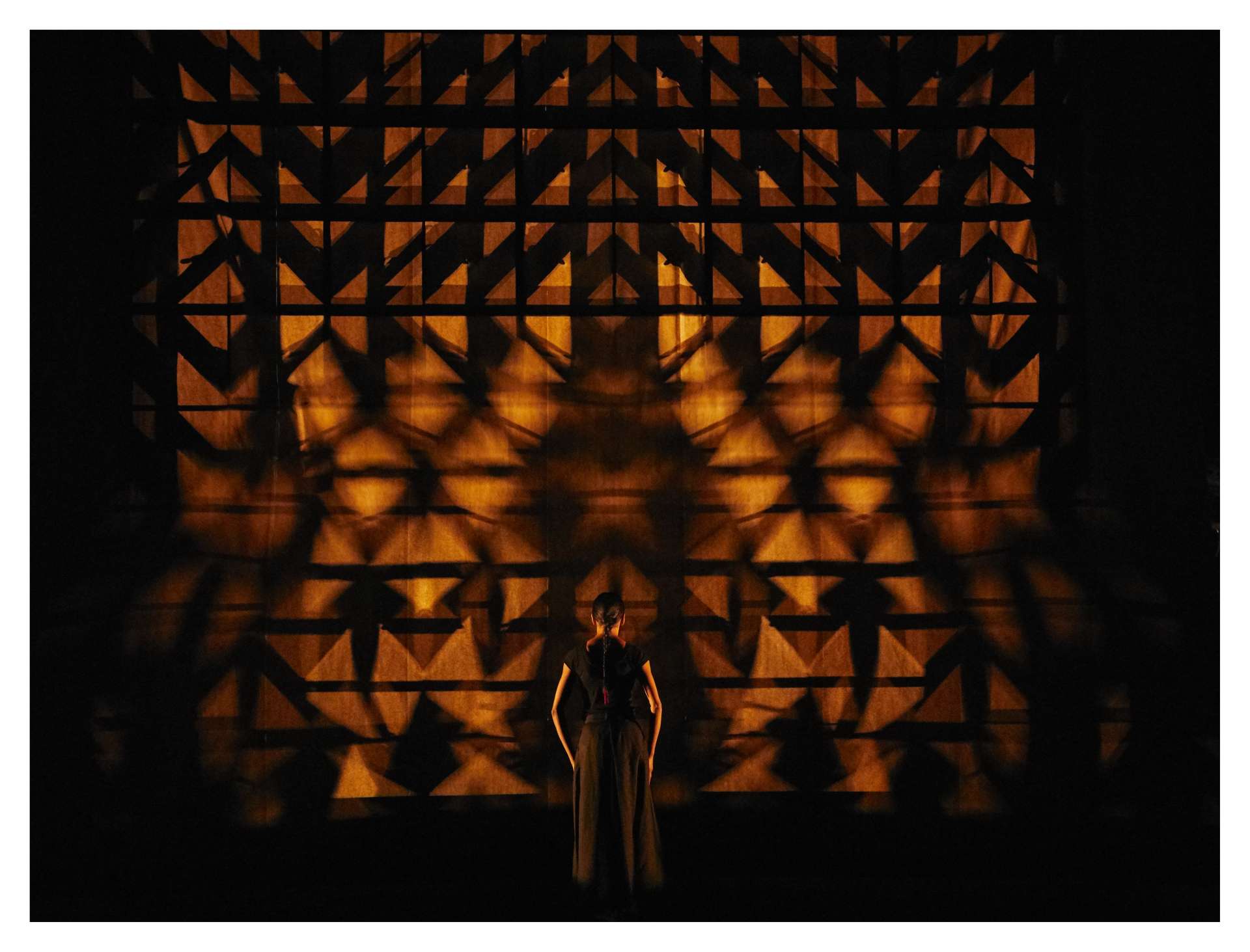 La danseuse Shantala Shivalingappa, de dos au public, est face à une projection visuelle et graphique. 