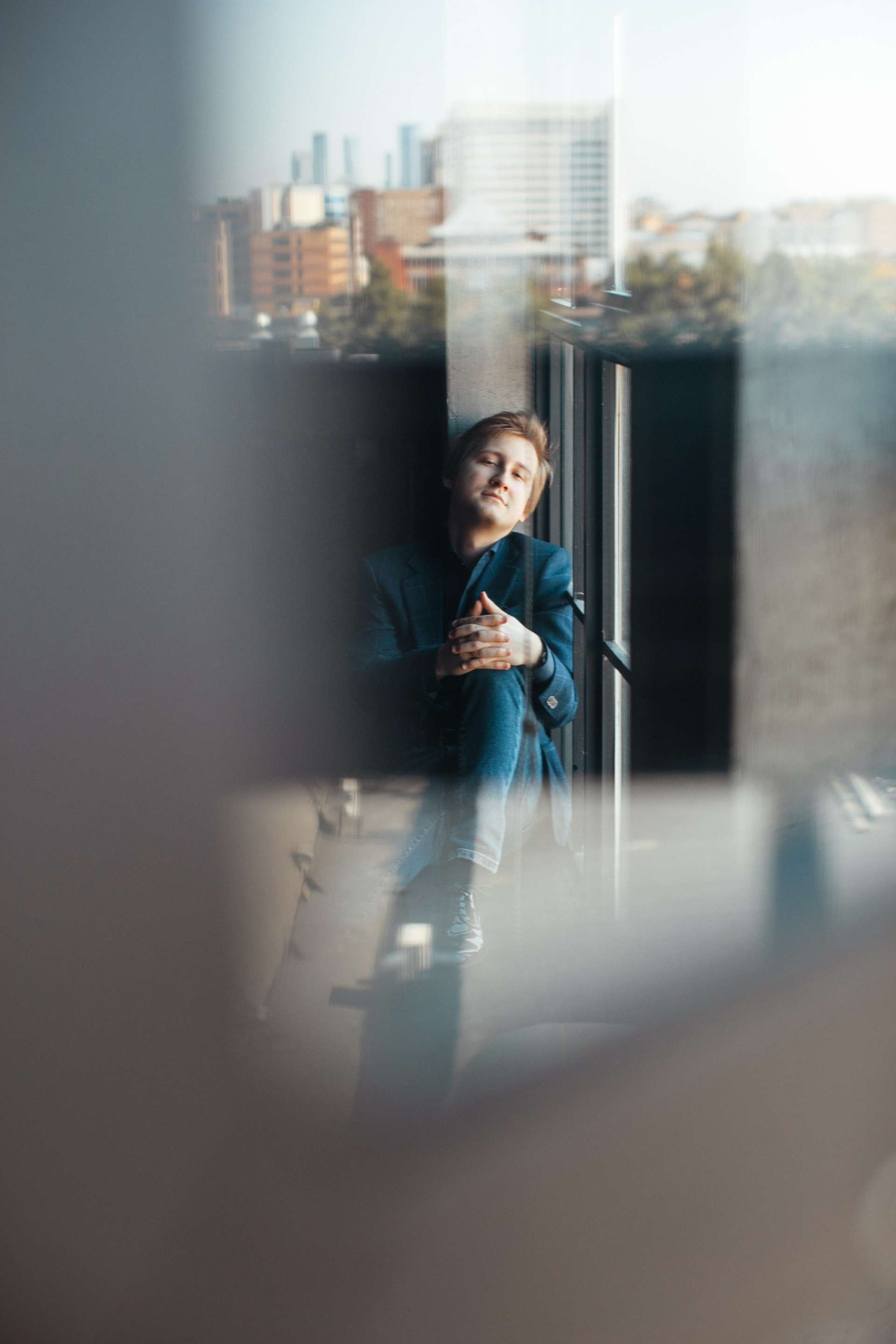 Dmitry Masleev pose pour un portrait de face. Un jeu de reflet montre des tours d'immeubles au loin. 
