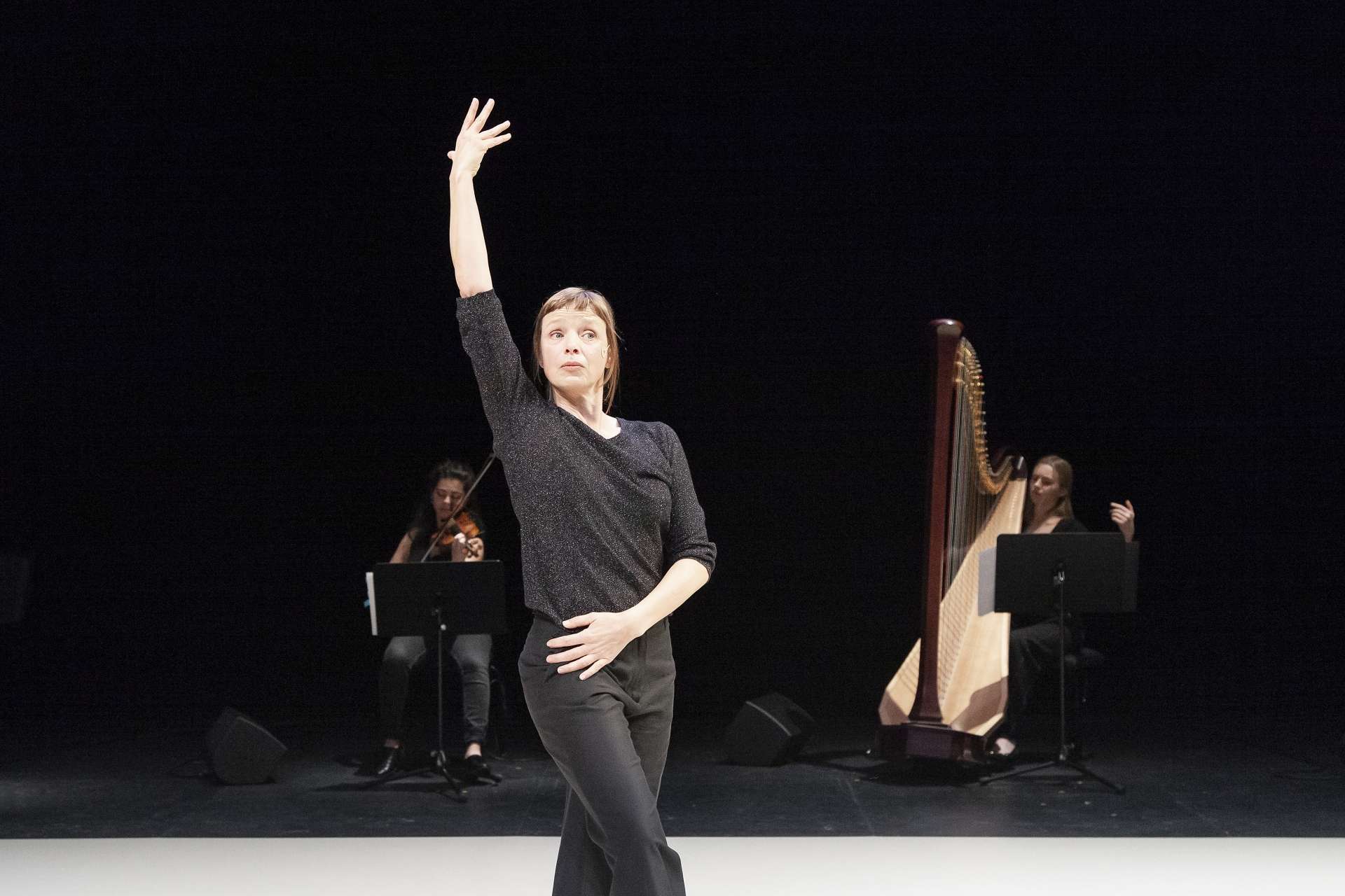 Samantha van Wissen, danseuse et interprète de Giselle..., effectue une posture de danse en bord de scène alors que deux musiciennes jouent en fond de scène. 
