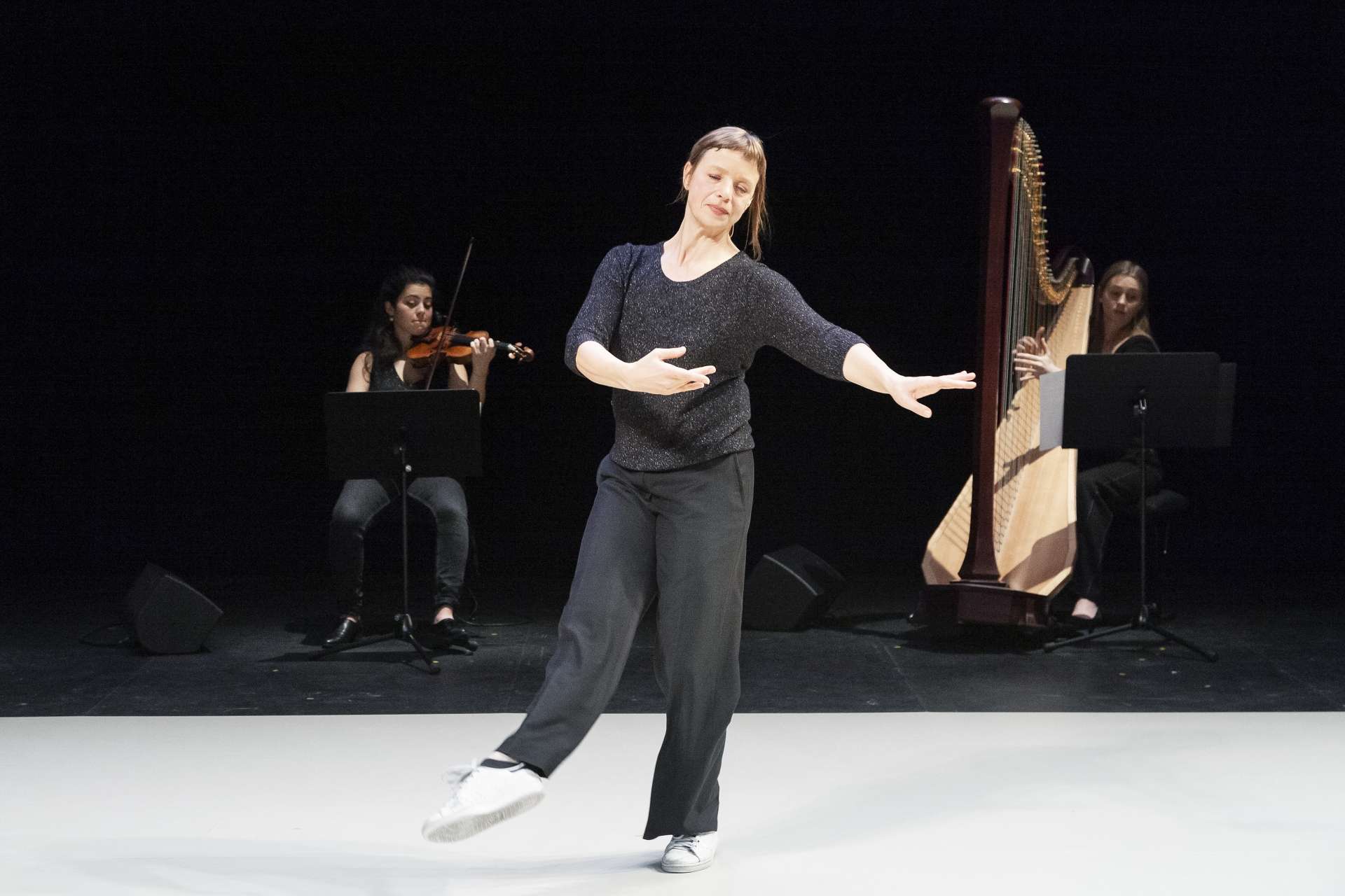 Samantha van Wissen, danseuse et interprète de Giselle..., effectue un mouvement dansé en bord de scène alors que deux musiciennes jouent en fond de scène. 