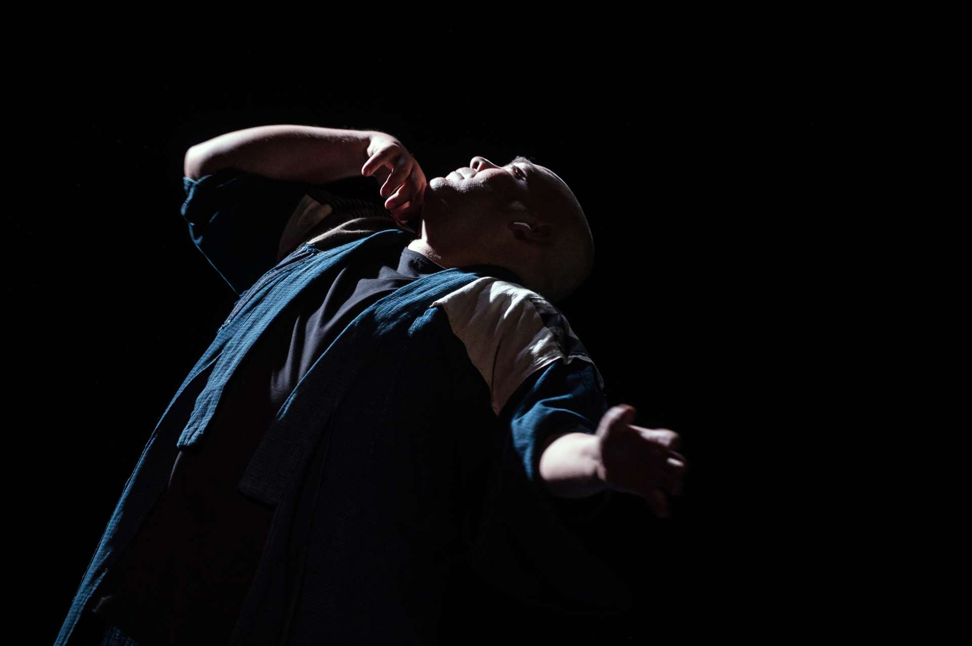 Portrait de Thomas Lebrun en train de danser, buste incliné et tête en arrière, une main tendue sur le côté et une main levée et repliée. 