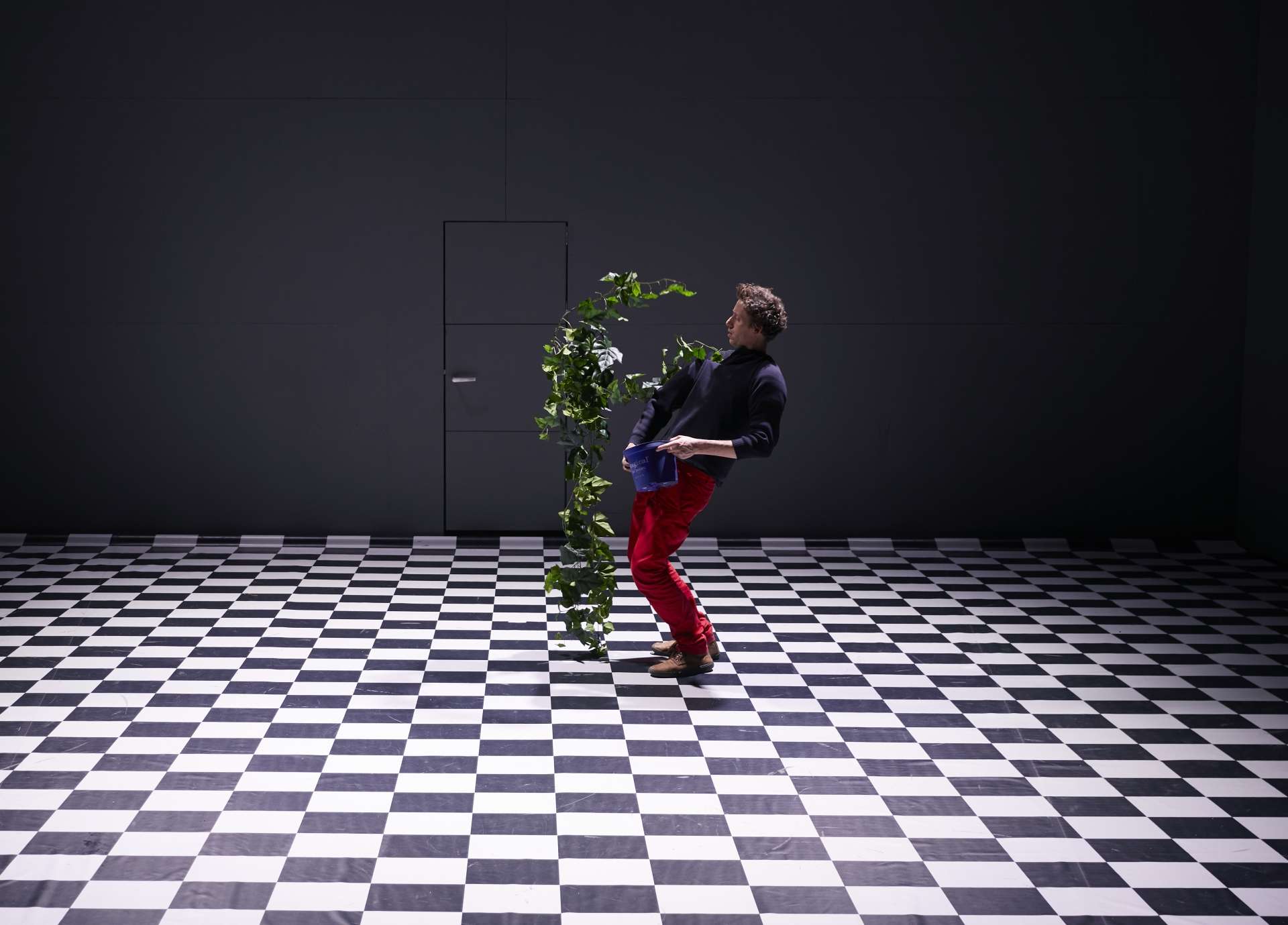 Sol en damier noir et blanc, un homme seul est situé au milieu. Il est en plein corps à corps avec une plante géante. 