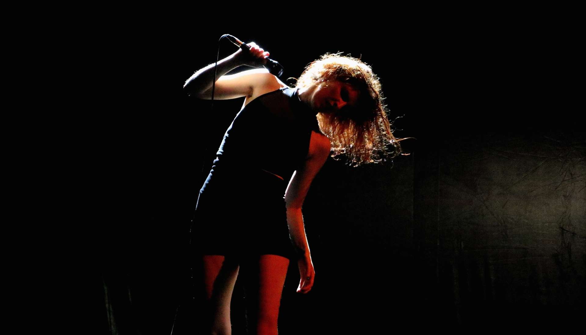 Sarah Espour en robe noir et suspendue à son micro.