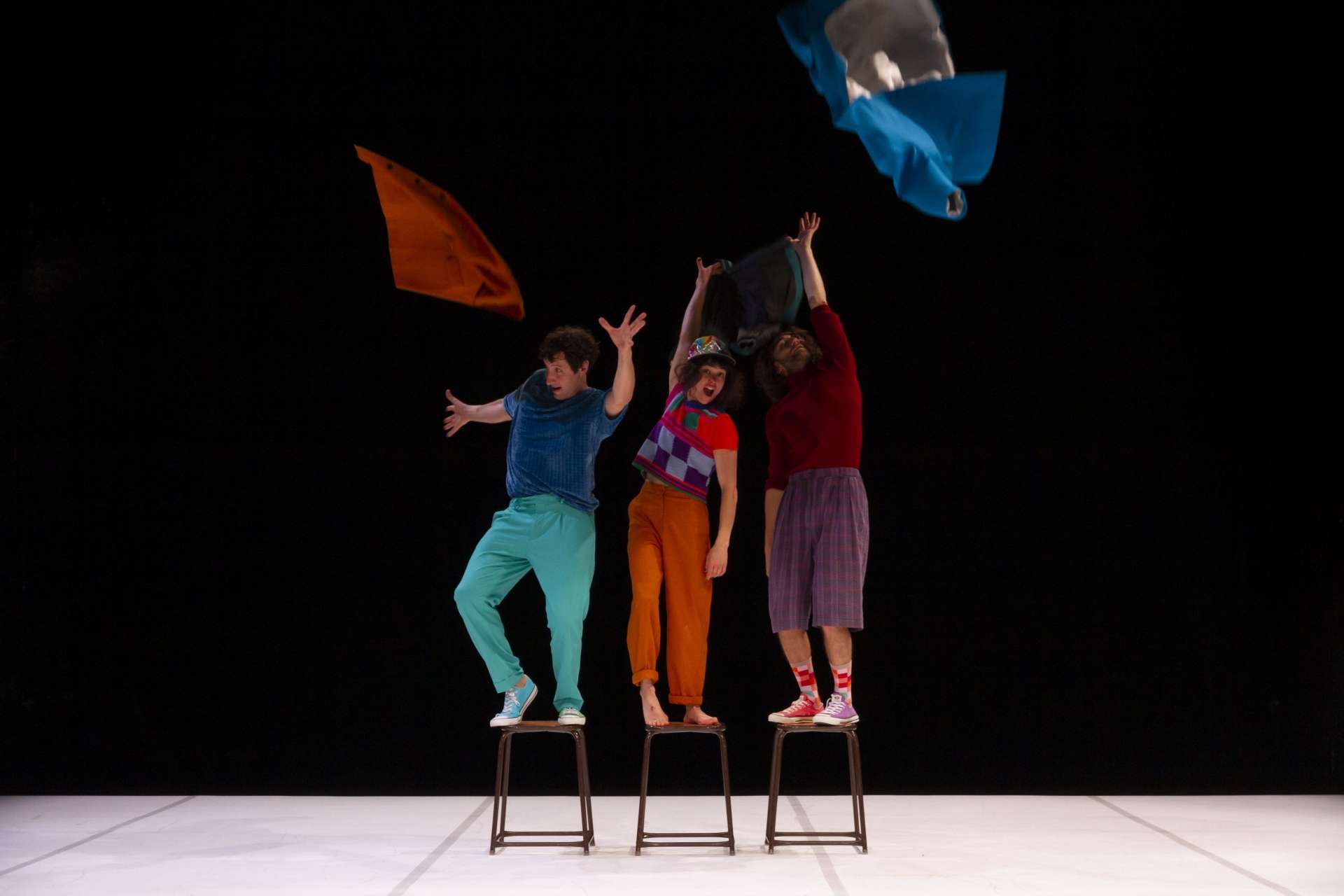 Les trois interprètes du spectacle debout sur des tabourets, un tissu à la main. 