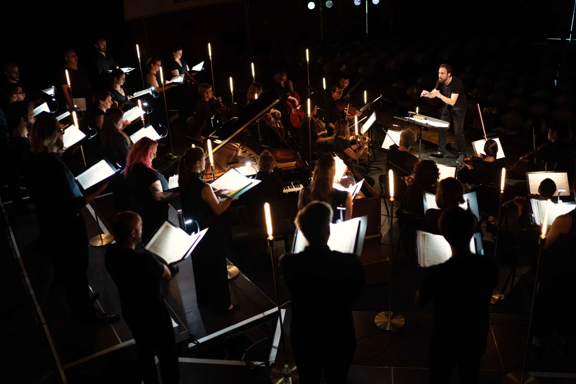 De dos, les 46 musiciens et musiciennes installés en demi-cercle font face au chef d'orchestre Simon-Pierre Bestion. Celui-ci est en pleine action de direction. 
