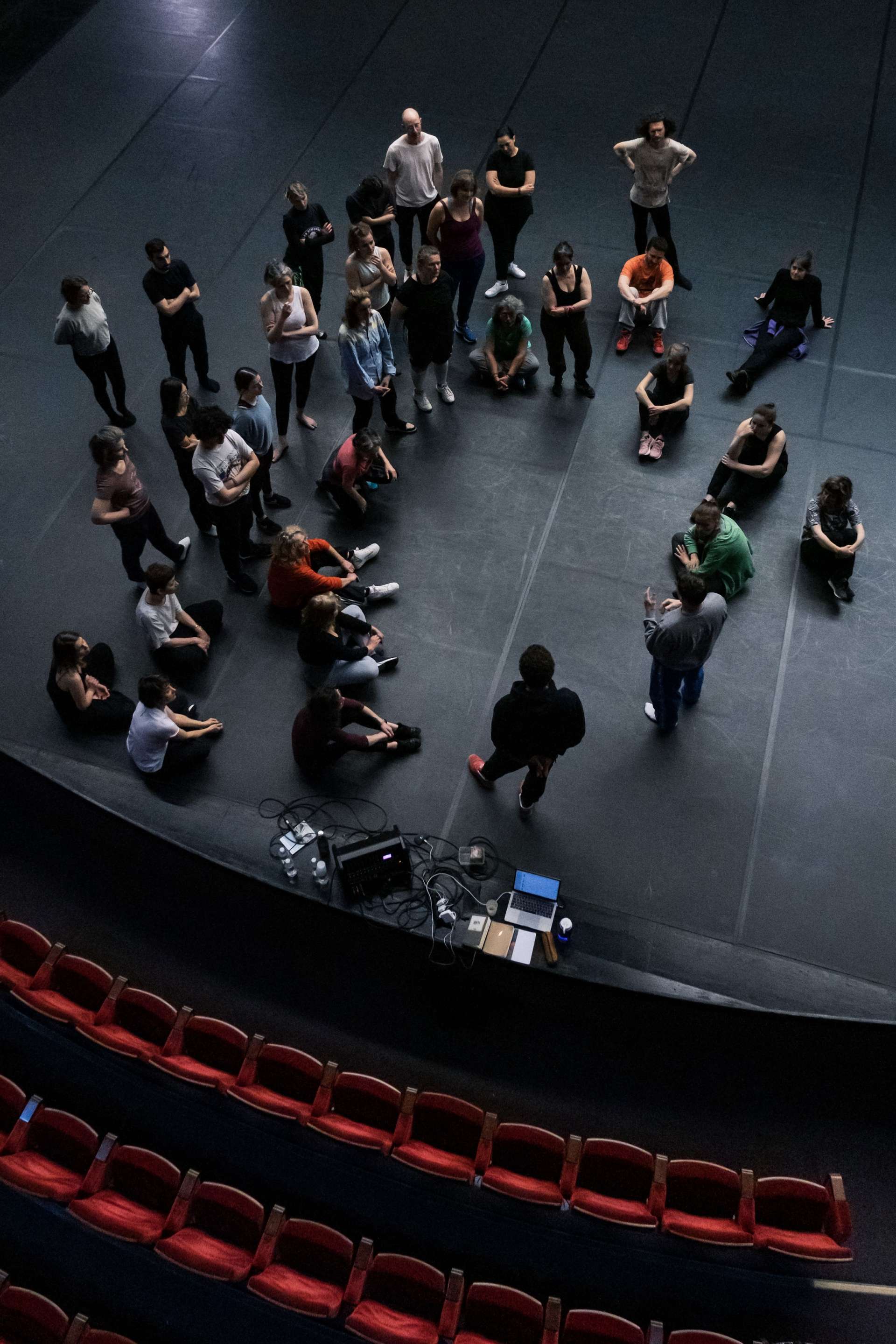 Bord de scène de la salle Touchard, un cercle de personnes est formé autour d'une artiste. 
