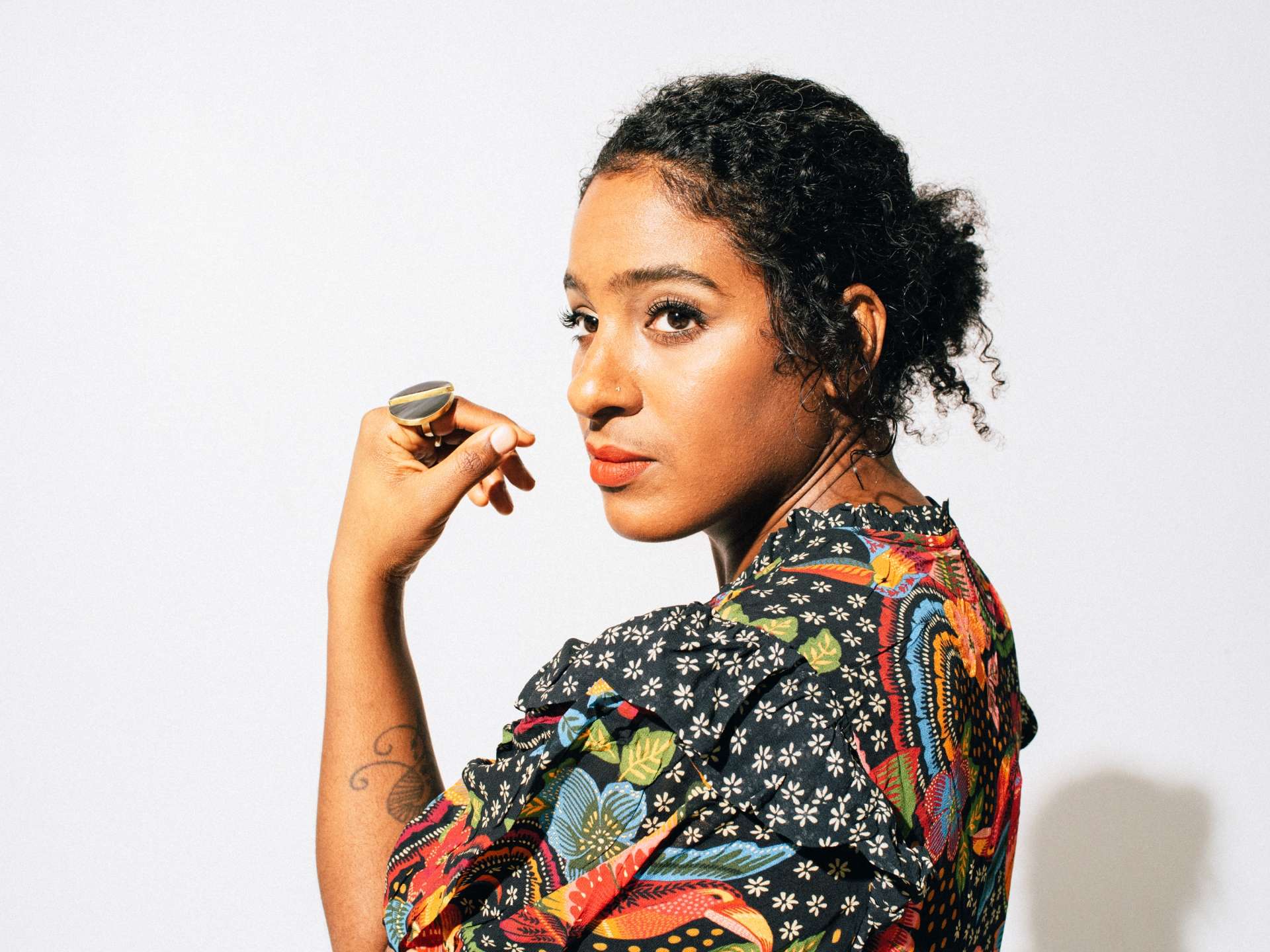 Portrait posé, de fprofil, de l'artiste Leyla McCalla sur fond blanc et vêtue d'une tenue colorée. 