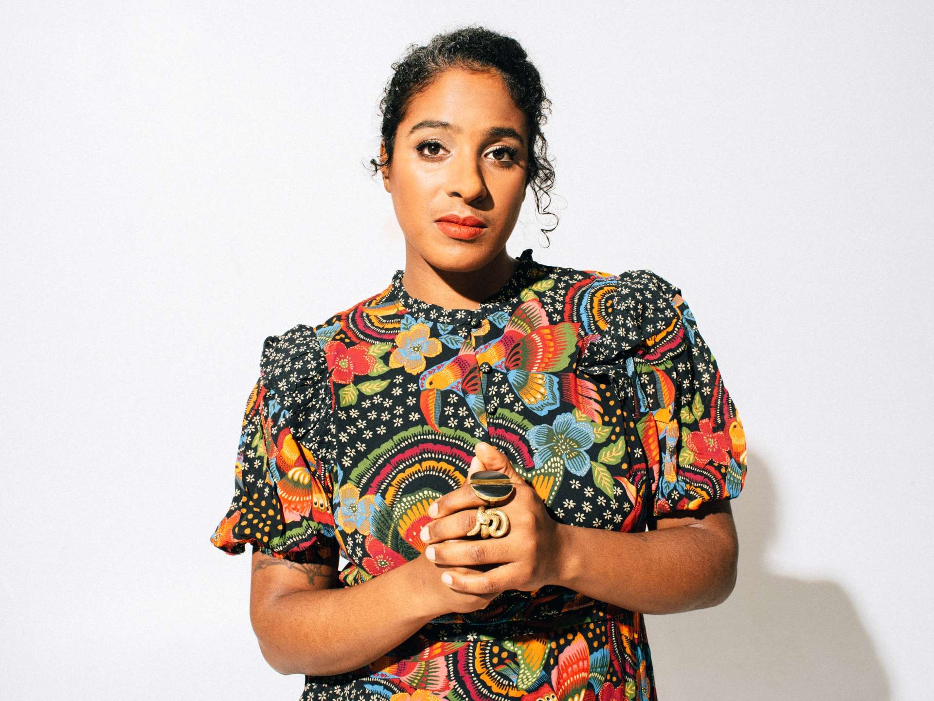 Portrait posé, de face, de l'artiste Leyla McCalla sur fond blanc et vêtue d'une tenue colorée. 