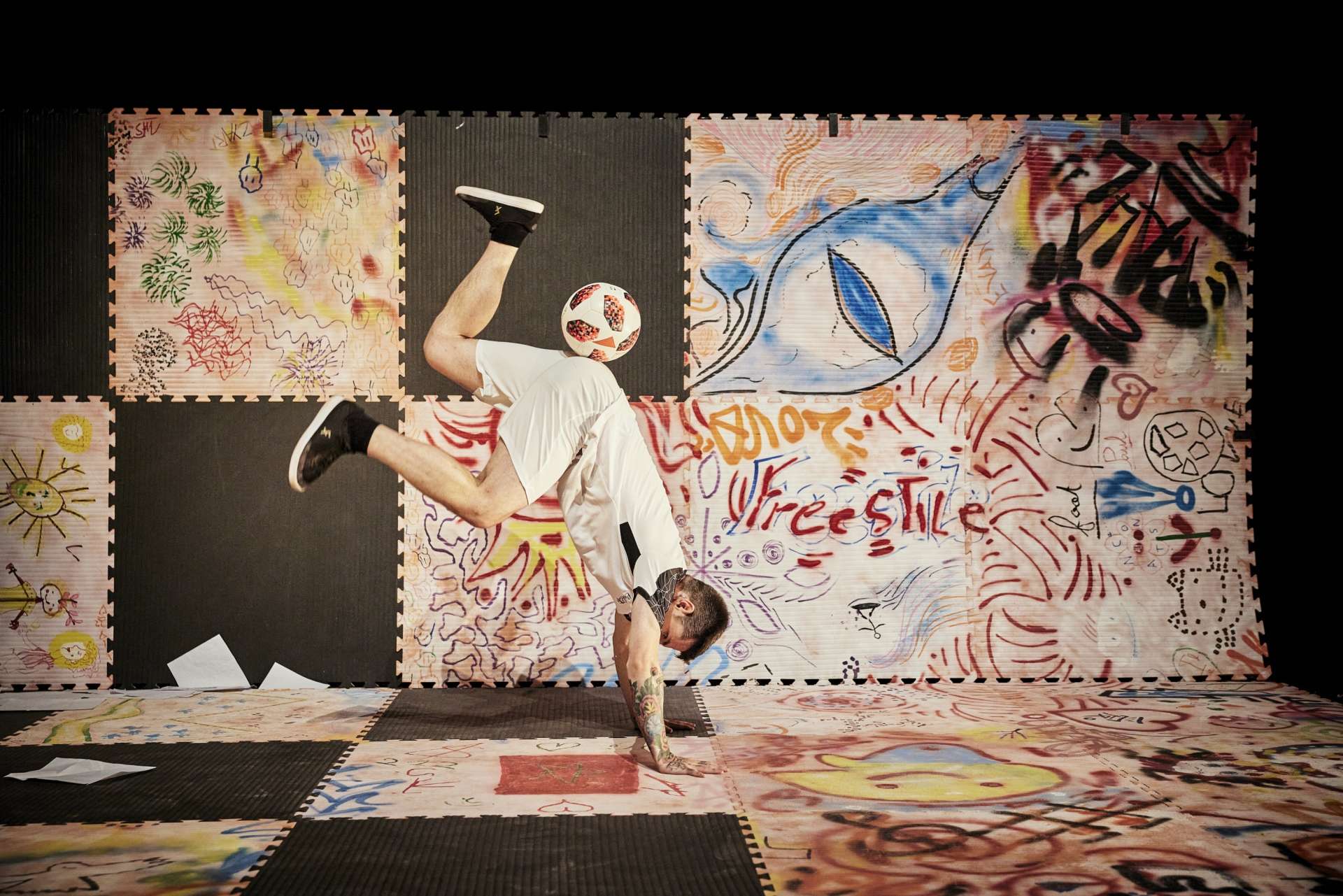 Dans un décor fait de dalles de sport, dont certaines sont graffées, Paul Molina réalise une figure de foot freestyle. Tête en bas, en équilibre sur ses mains et les pieds en l'air. 