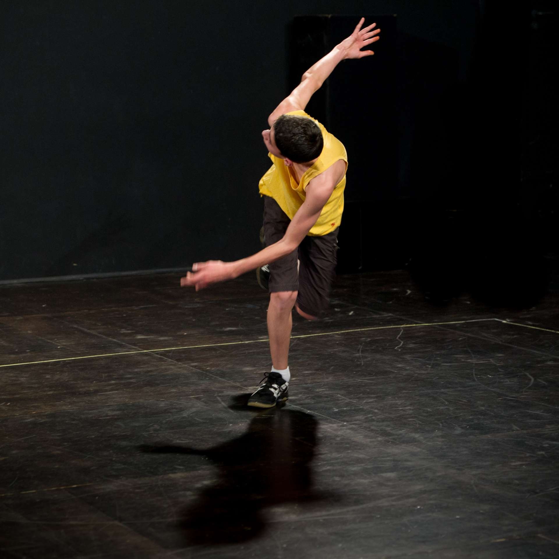 Un adolescent, habillé d'une marcel jaune et d'un short noir, danse. 