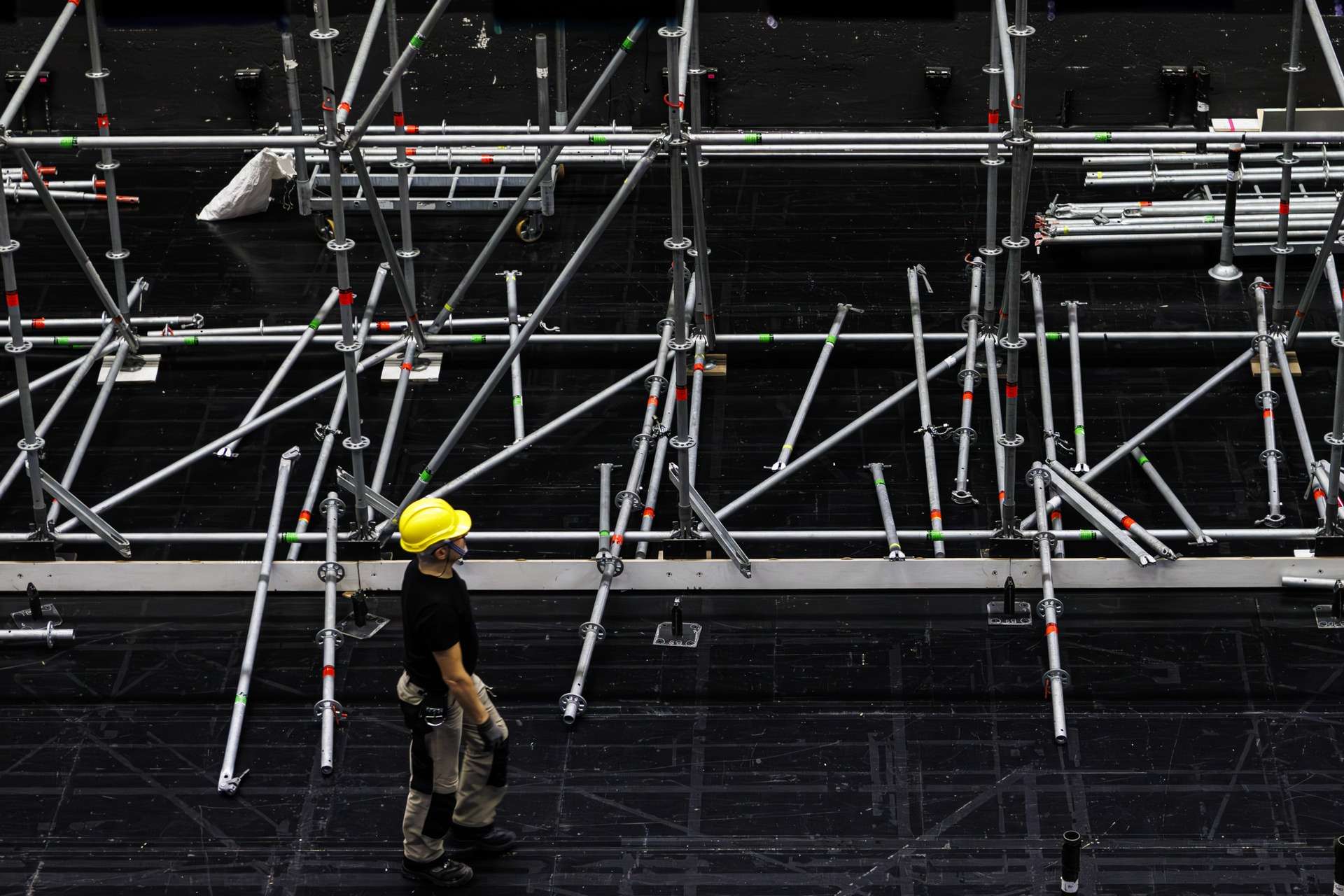 Technicien marchant sur le plateau, devant un échafaudage en construction. Des moises sont dispatchés par terre.