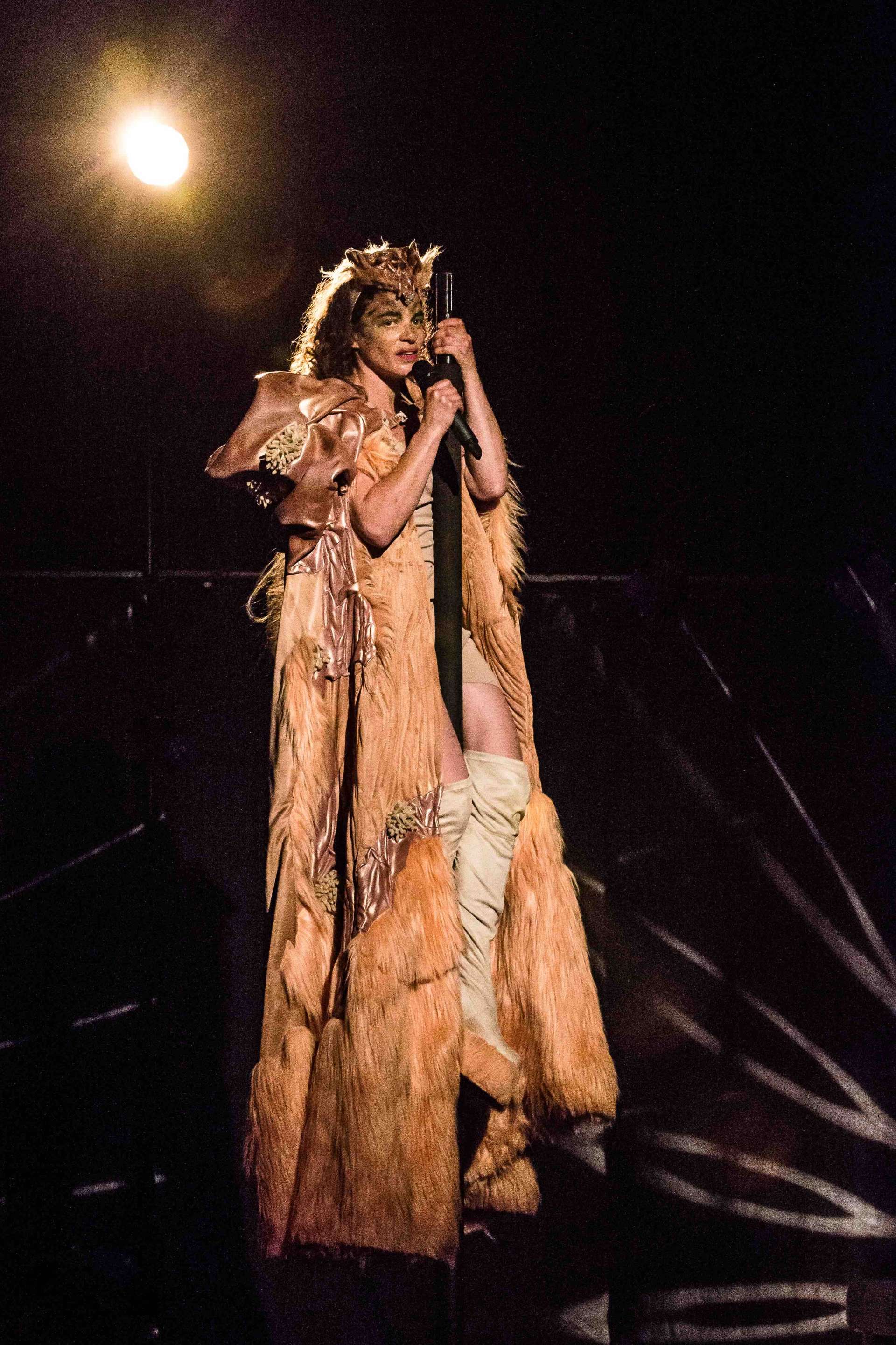 Juglair micro en main est perchée sur mât chinois. Droite, elle est vêtue d'un incroyable costume, teinte chair, fait de fourrure et de satin et portent une paire de cuissardes beiges. . 
