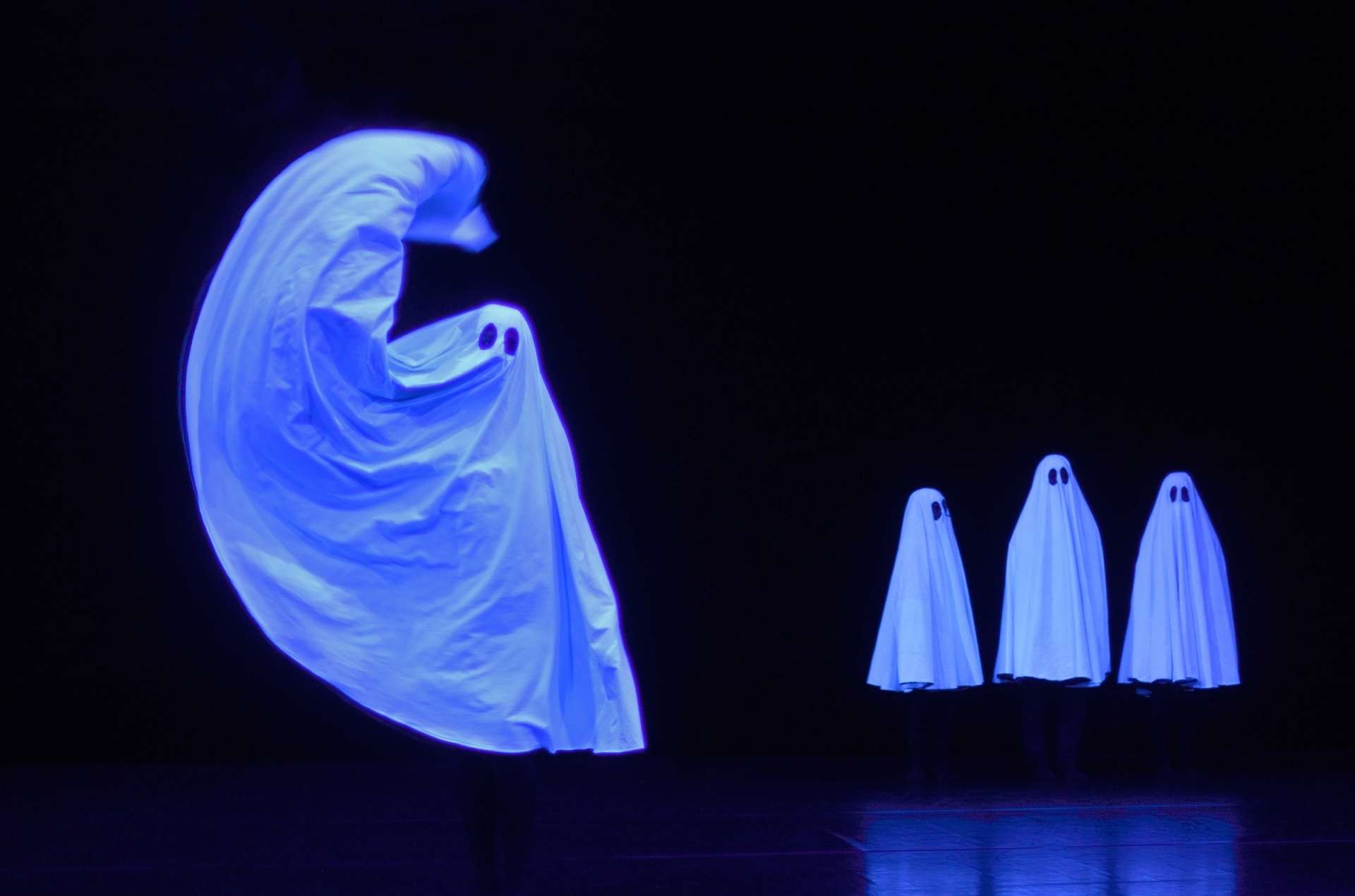 Fond noir. Quatre fantômes illuminent par la blancheur de leurs costumes. 