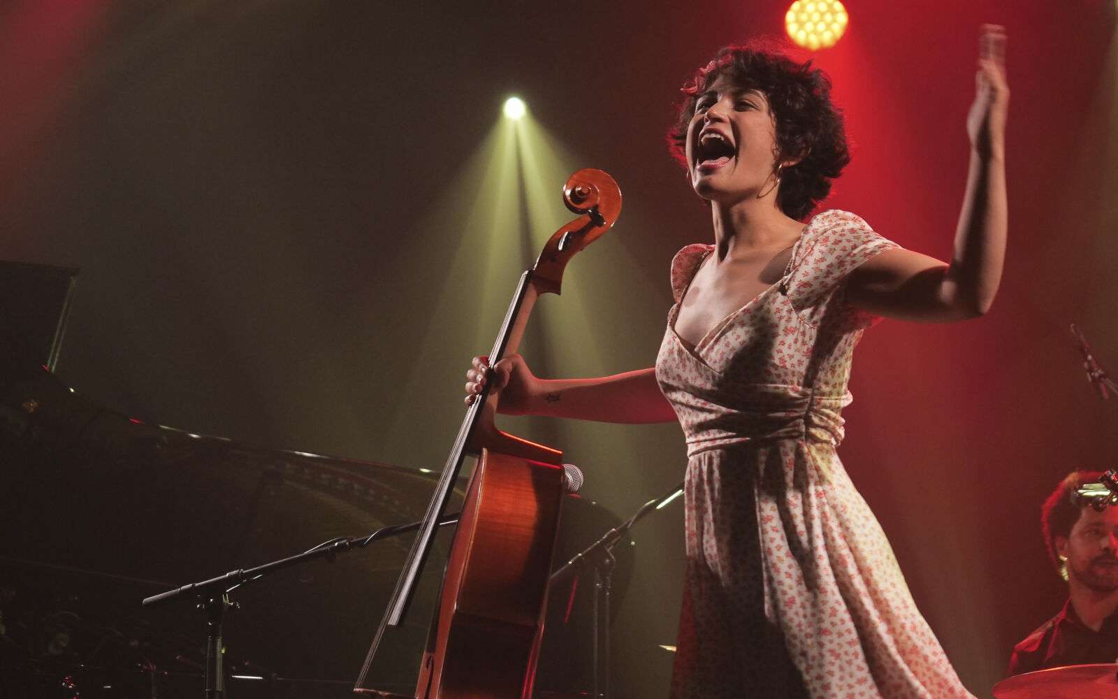 Sur scène, portrait de la chanteuse Ana Carla Maza en robe printanière et violoncelle en main. 