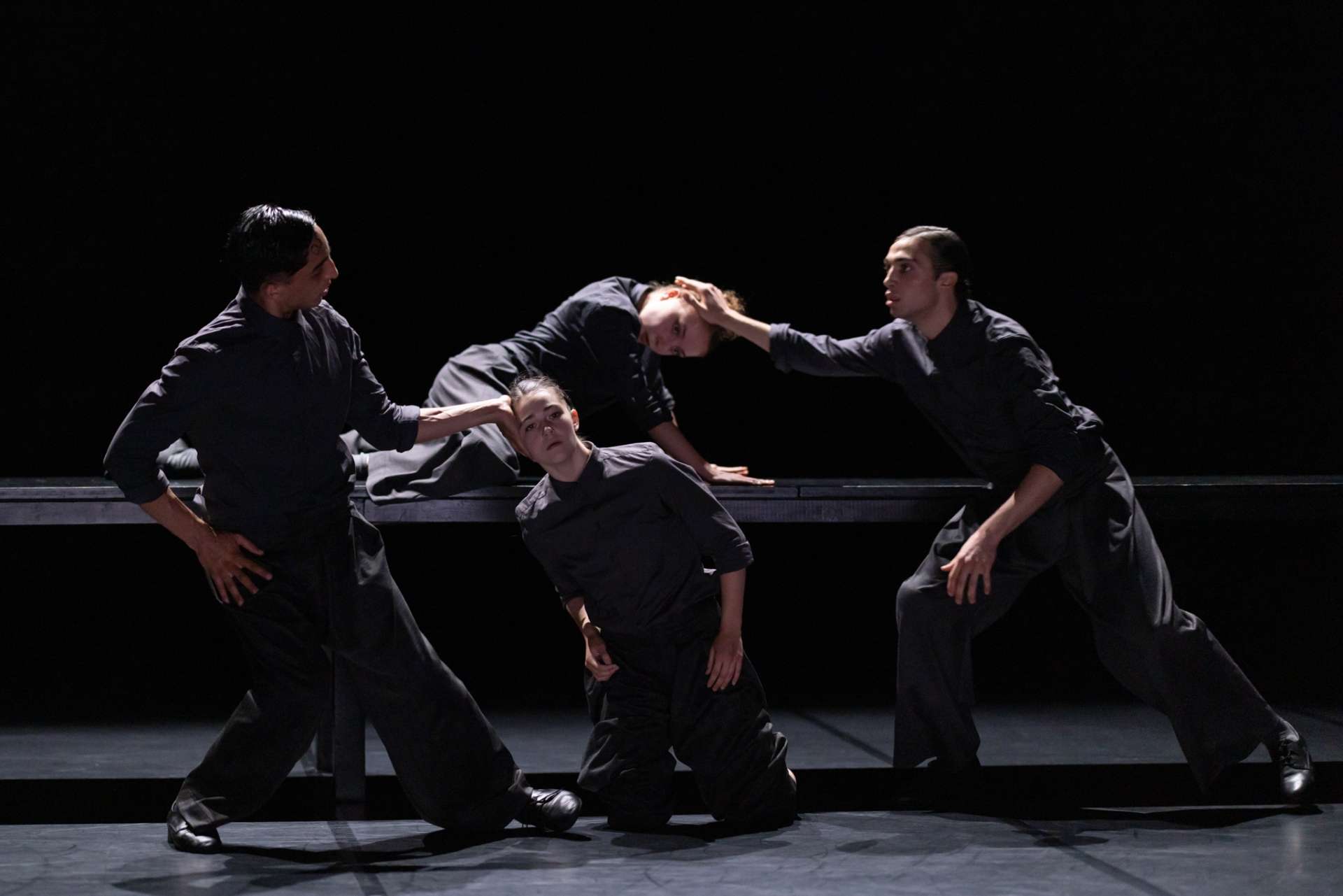 En tenues noires, dans la pénombre, quatre interprètes dansent par binôme homme et femme. 