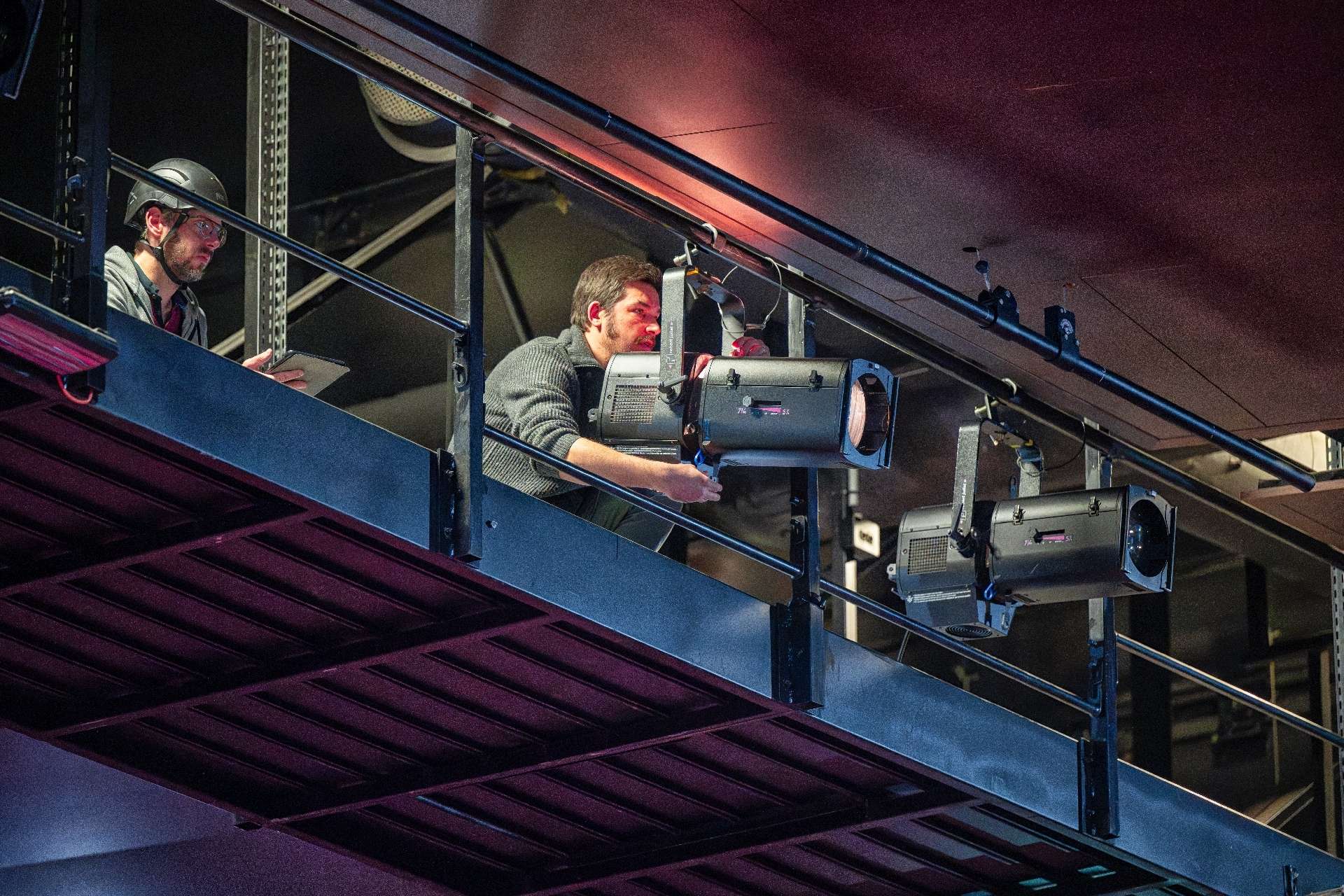 Deux régisseurs lumières installent des projecteurs sur la passerelle.