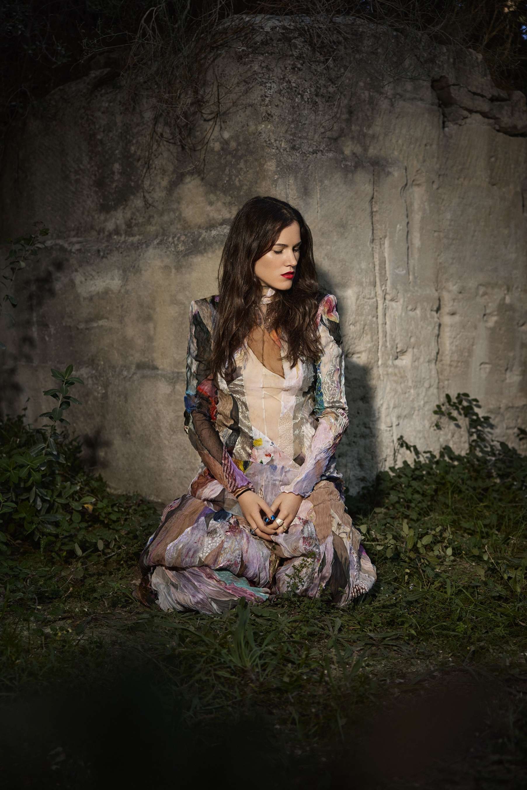 Portrait de la chanteuse Clara Ysé dans une robe fleurie en extérieur dans de la verdure et face à un mur en béton. 