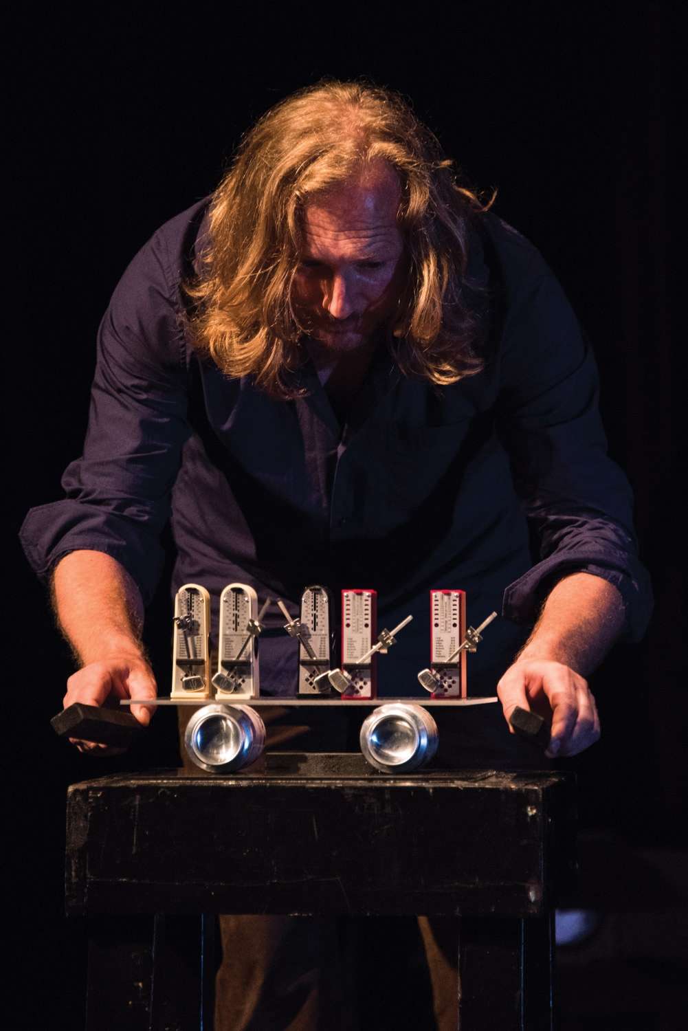 Portrait du magicien Kurt Demey en train de manipuler des métronomes. 