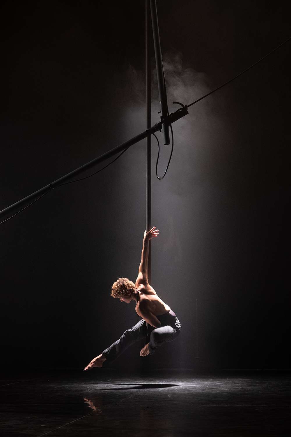 Tel un ange suspendu, un acrobate est accroché en l'air. Le halo de lumière met en valeur sa chevelure blonde. 
