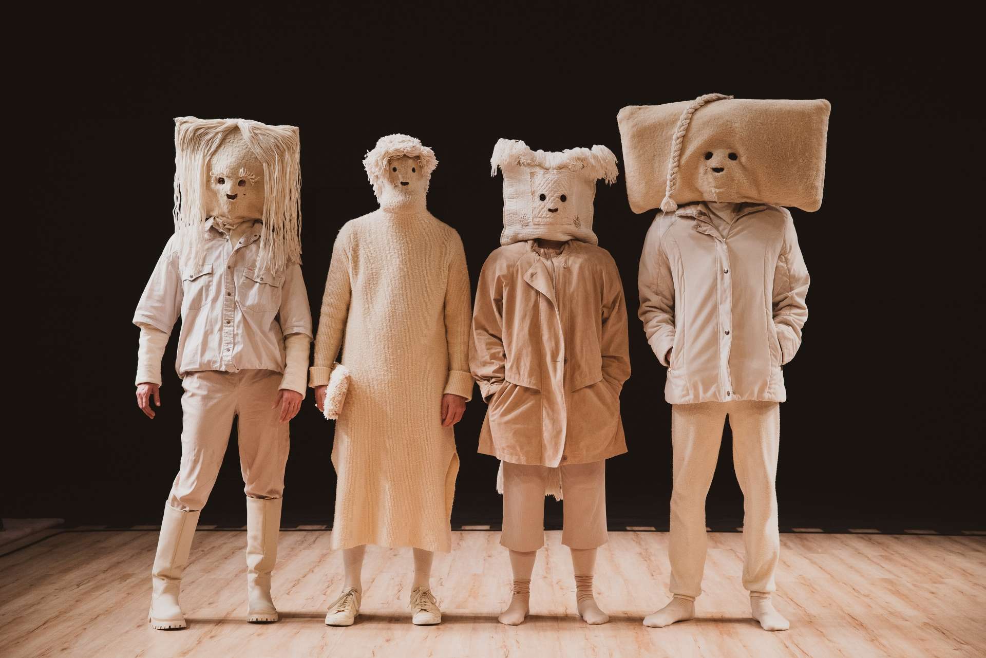 Quatre drôles de personnages posent de face. Ils sont habillés en beige avec des costumes farfelus.