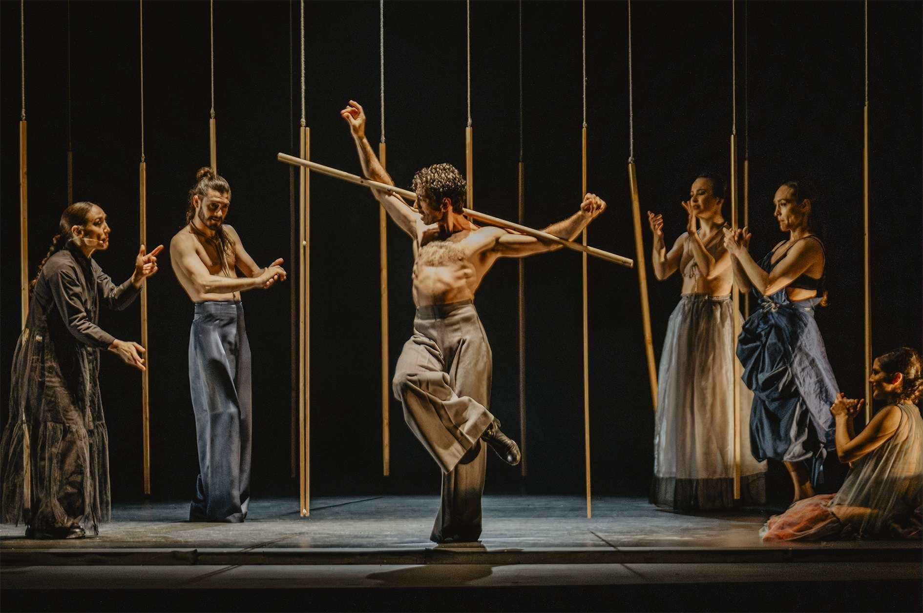 Au premier plan, le danseur de flamenco David Coria. Pantalon à pinces, torse nu, baton coincé entre les bras, il danse devant cinq autres interprètes. En fond de scène, le décor est composé des mêmes bâtons. 