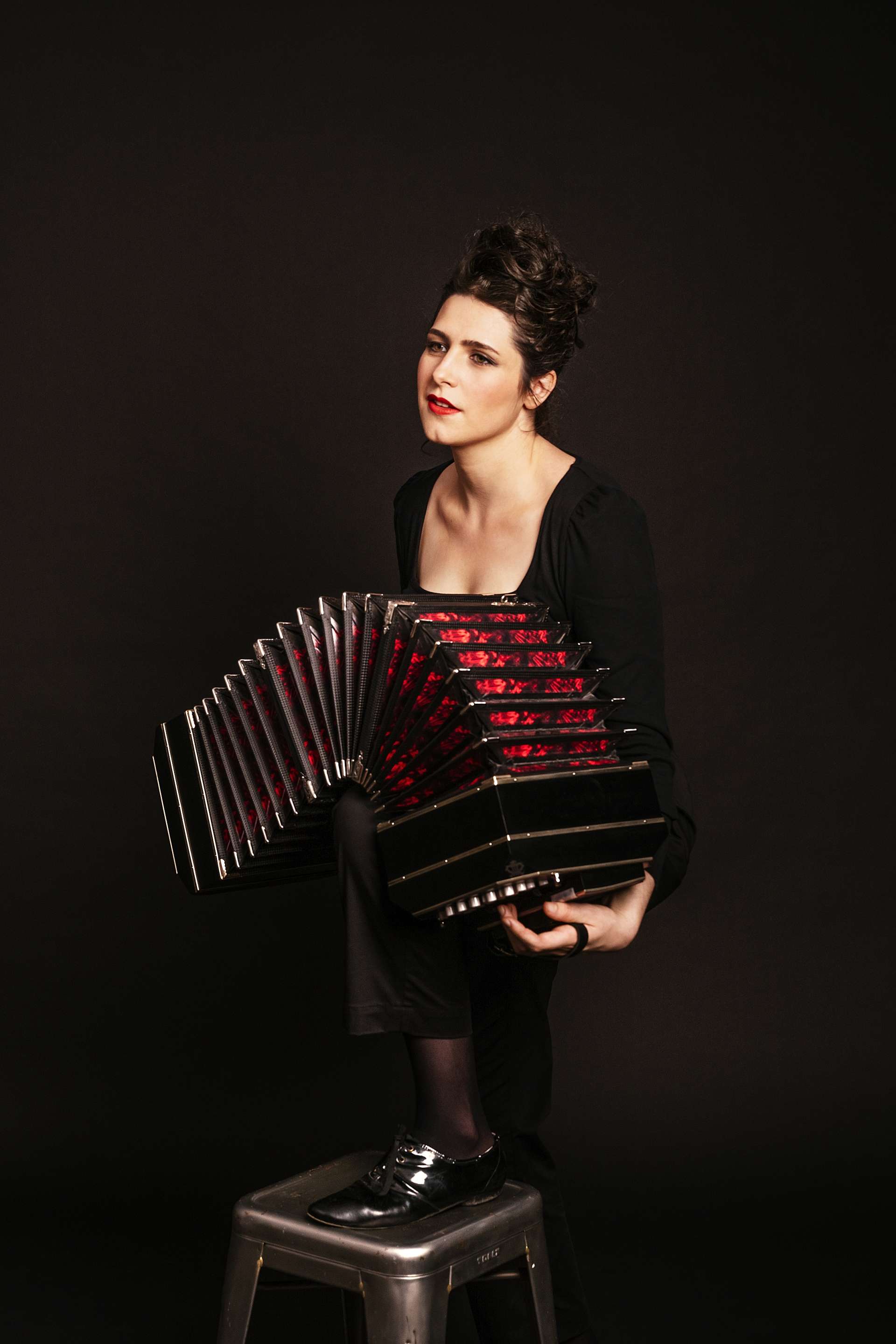 Sur fond noir, Louise Jallu pose avant son bandonéon aux soufflets rouges. 