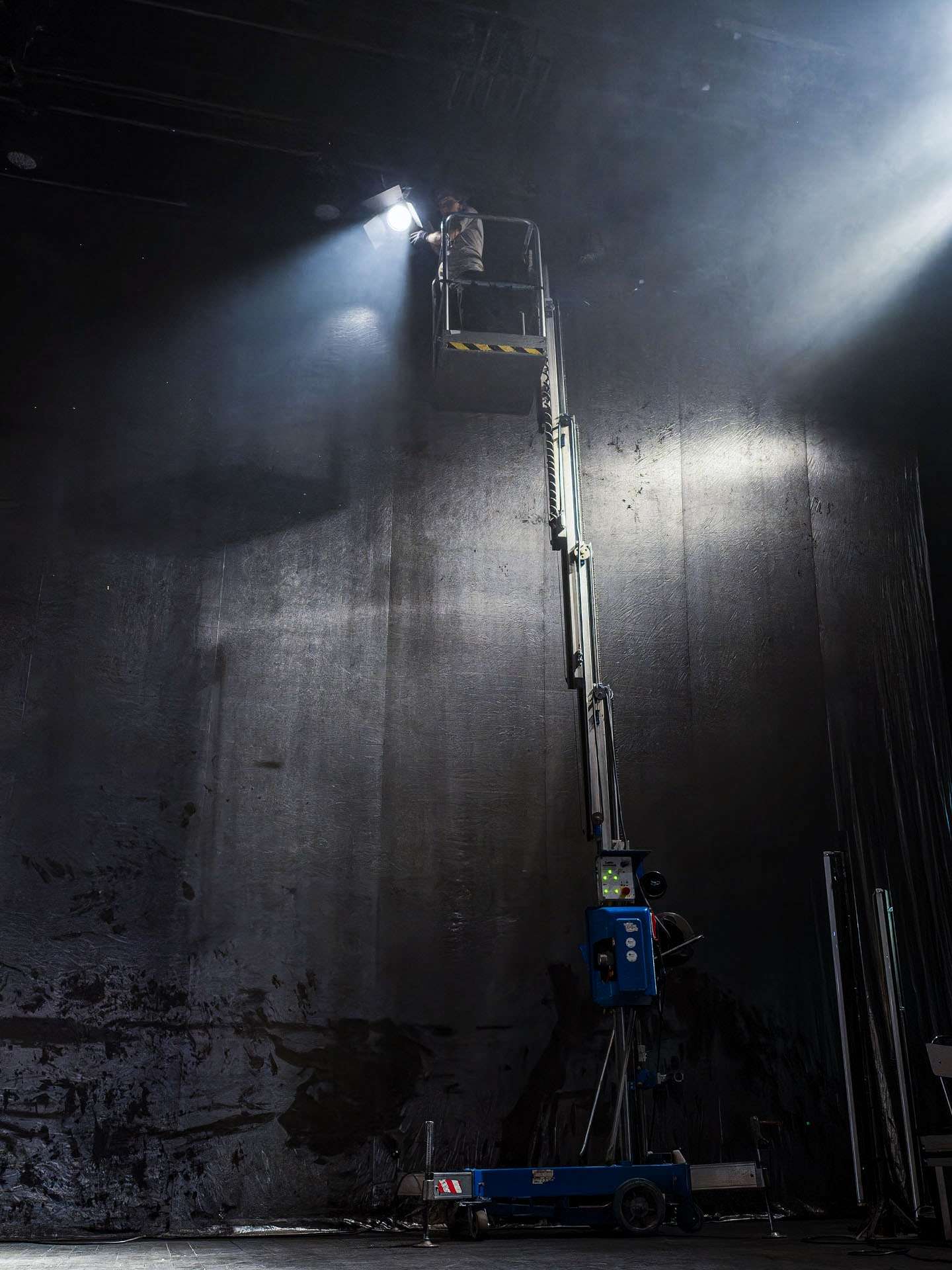 Technicien lumière réglant un projecteur en hauteur dans une nacelle.