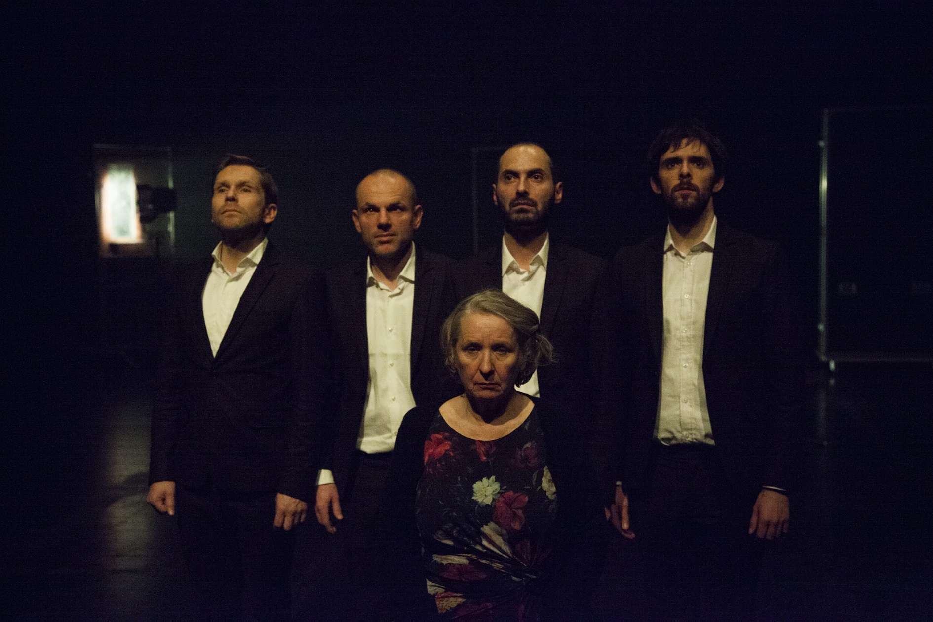 Portrait d'une femme avec, juste derrière elle, quatre hommes en costume et chemise blanche. 
