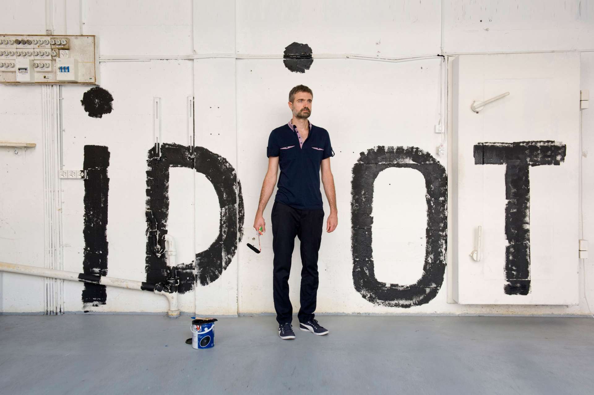 Personnage debout devant un mur. Inscription du mot IDIOT