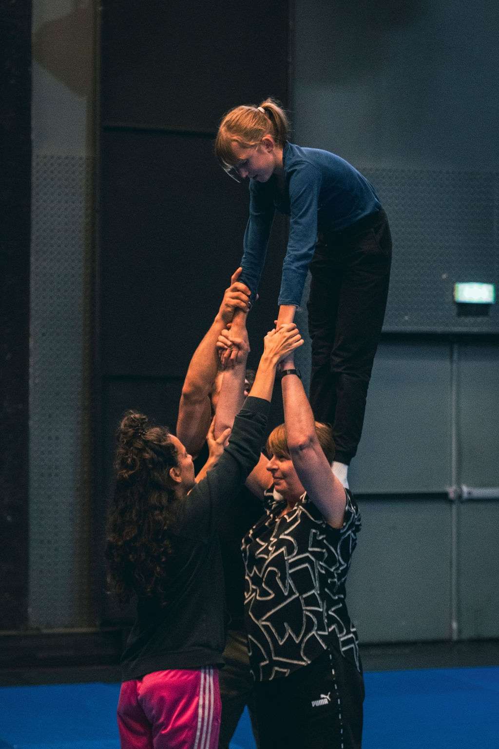 Une jeune fille en équilibre au sommet d'une pyramide humaine, soutenue par trois adultes lors d'un atelier de cirque