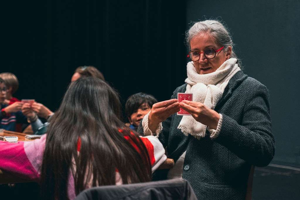 Lors d'un atelier cirque, une femme essaie un tour de magie avec des cartes à une jeune fille. 