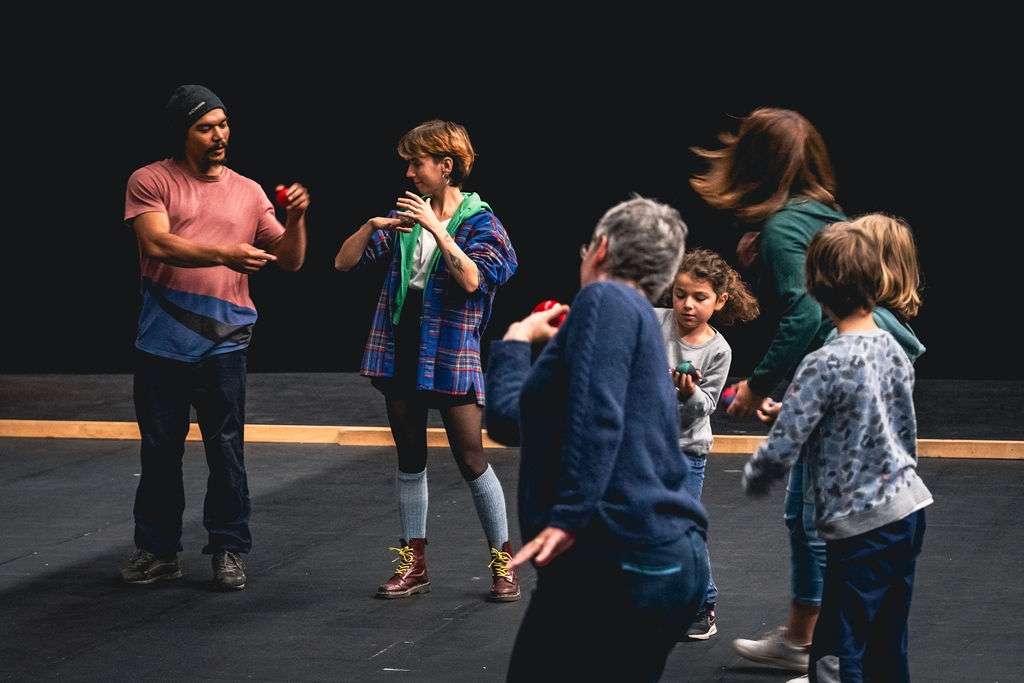 Des adultes et des enfants debout en cercle lors d'un atelier, jonglant avec des balles, concentrés sur leurs mouvements.