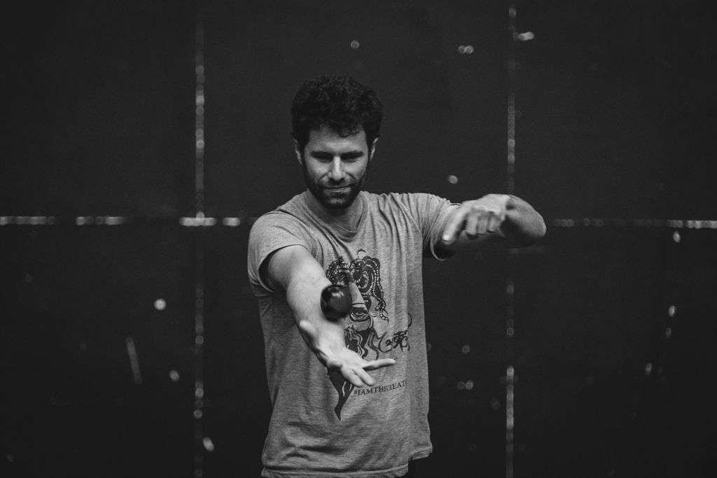 Photo monochrome, un homme debout lors d'un atelier, jonglant avec une balle en équilibre sur son bras, concentré sur son mouvement.