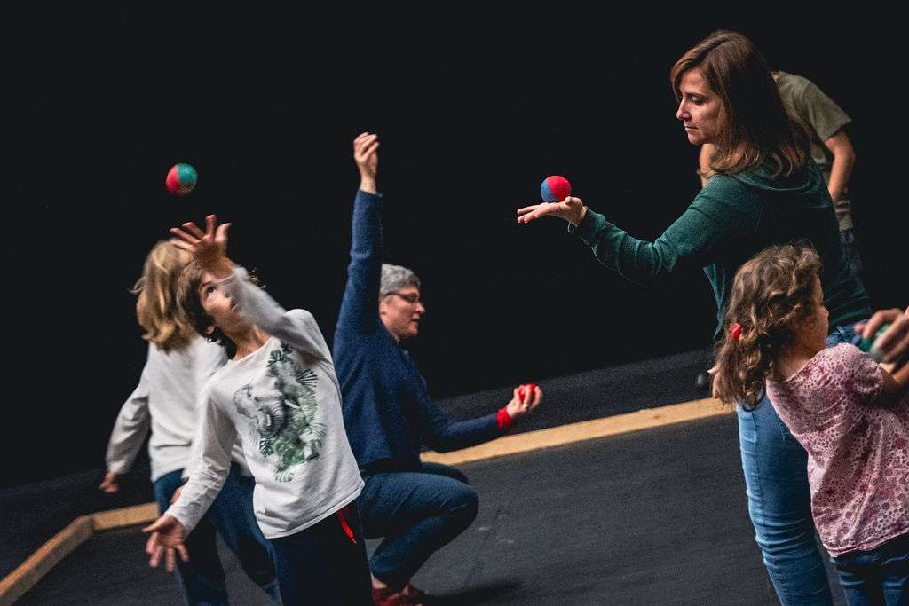 Des adultes et des enfants lors d'un atelier, testant le jonglage avec des balles, concentrés sur leurs mouvements.