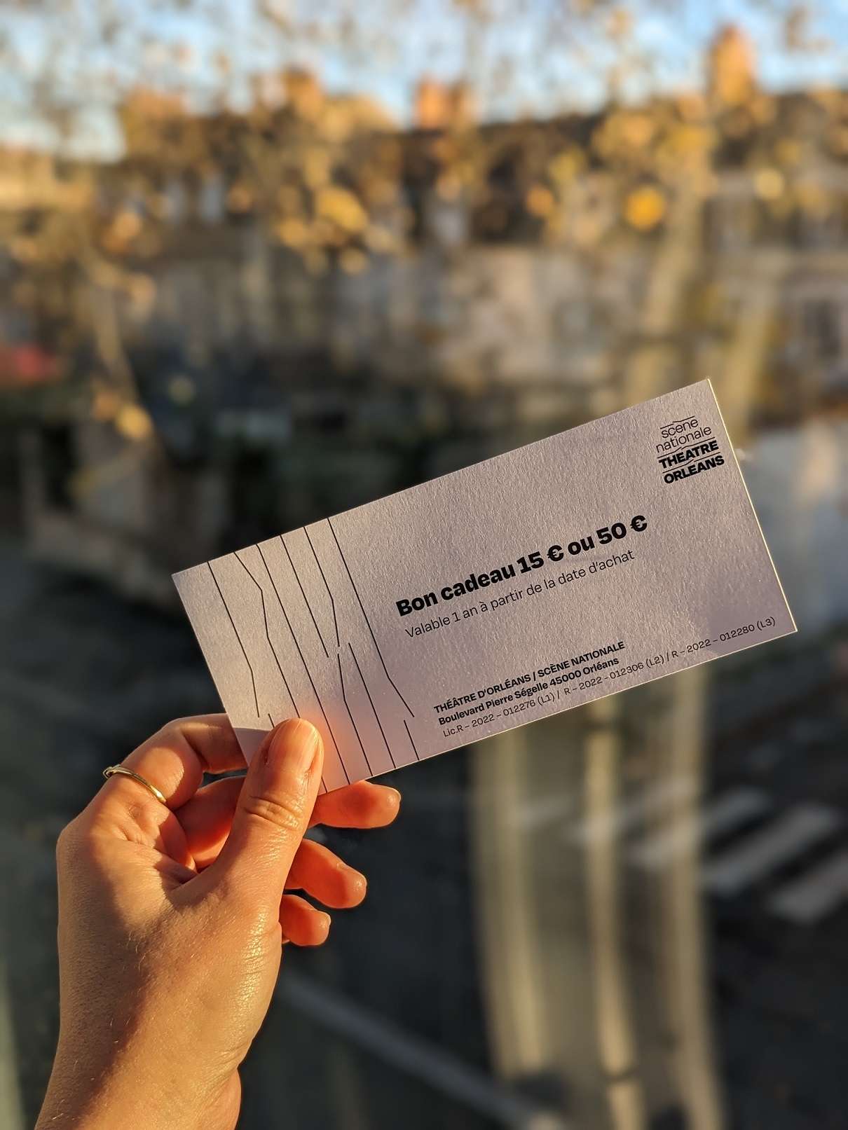 Une main gauche tient un billet cadeau en pleine lumière. 