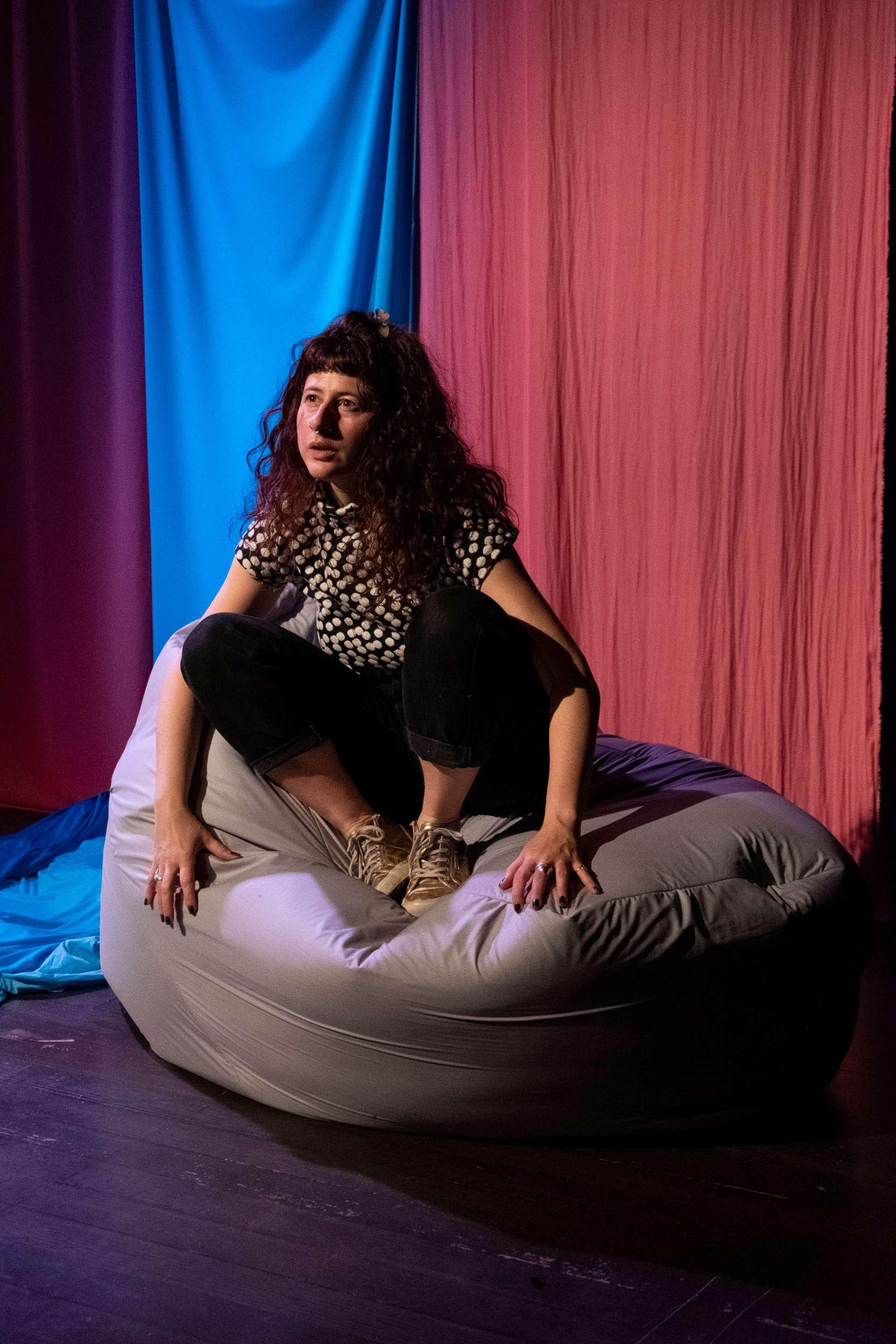 Pamina de Coulon est assise sur un pouf, elle regarde à son public, ses gestes reflètent ses paroles. Derrière elle on peut voir un drapé bleu, symbolisant une chute d'eau.
