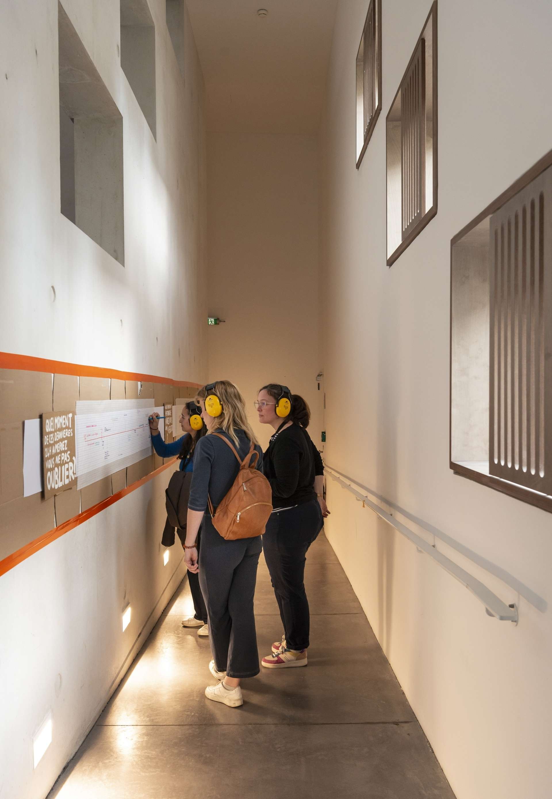 Dans un couloir, trois femmes observent des cartes accrochées au mur. 