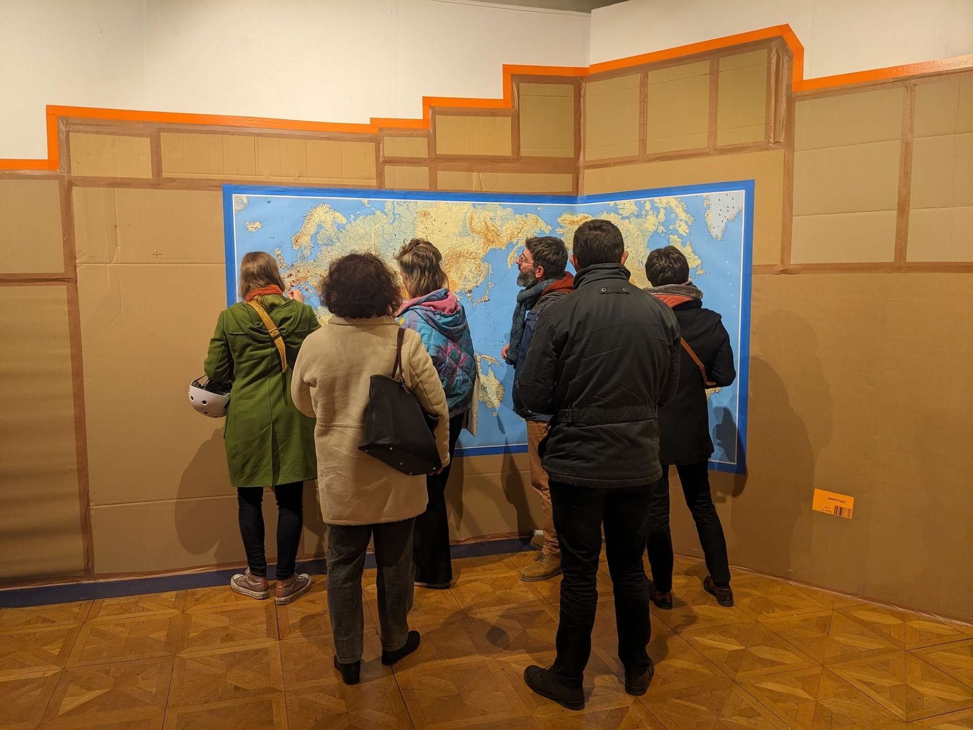 Sur un mur de cartons, une carte accrochée avec du public devant. 