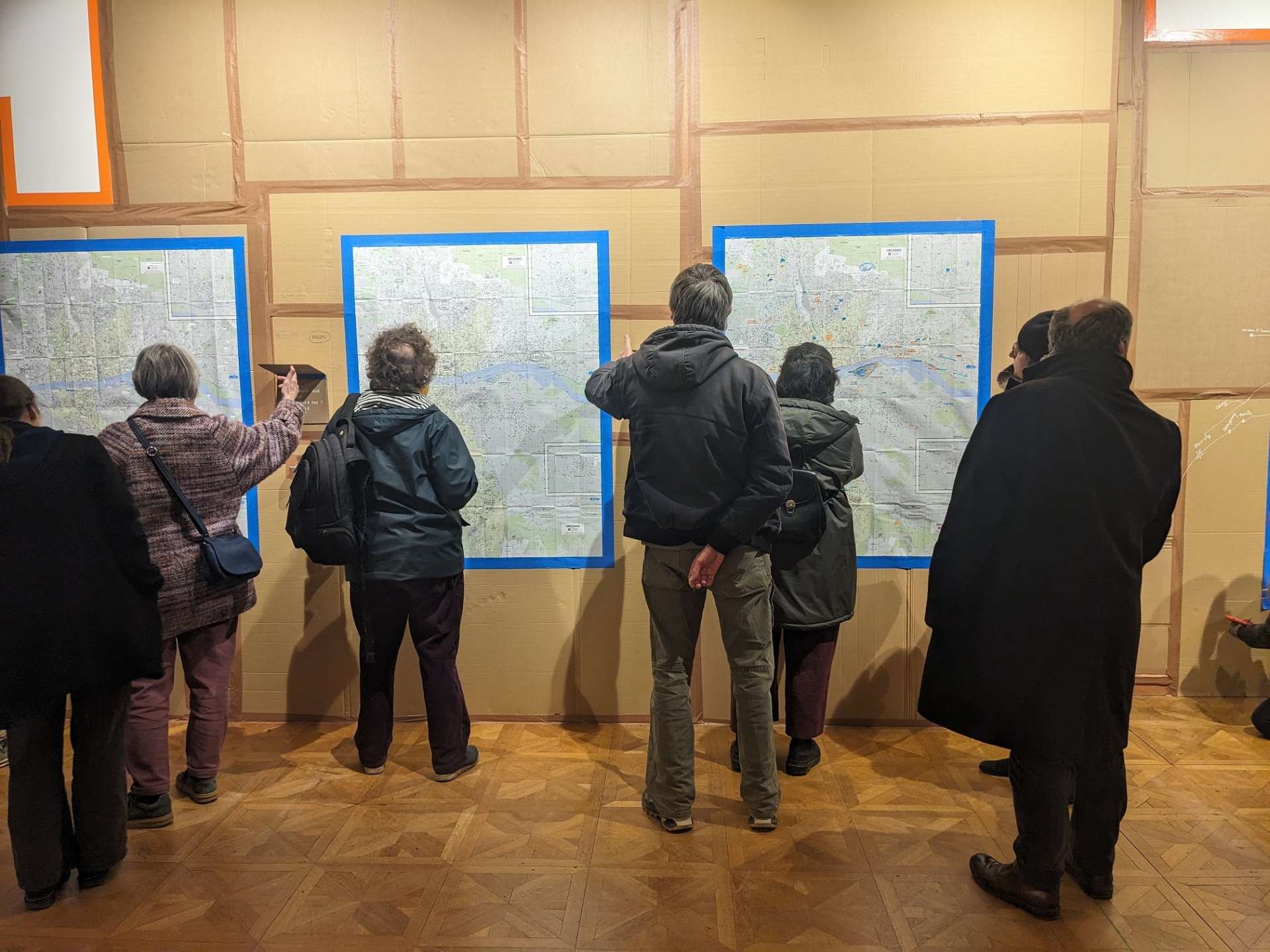 Sur un mur de cartons, une carte accrochée avec du public devant. 