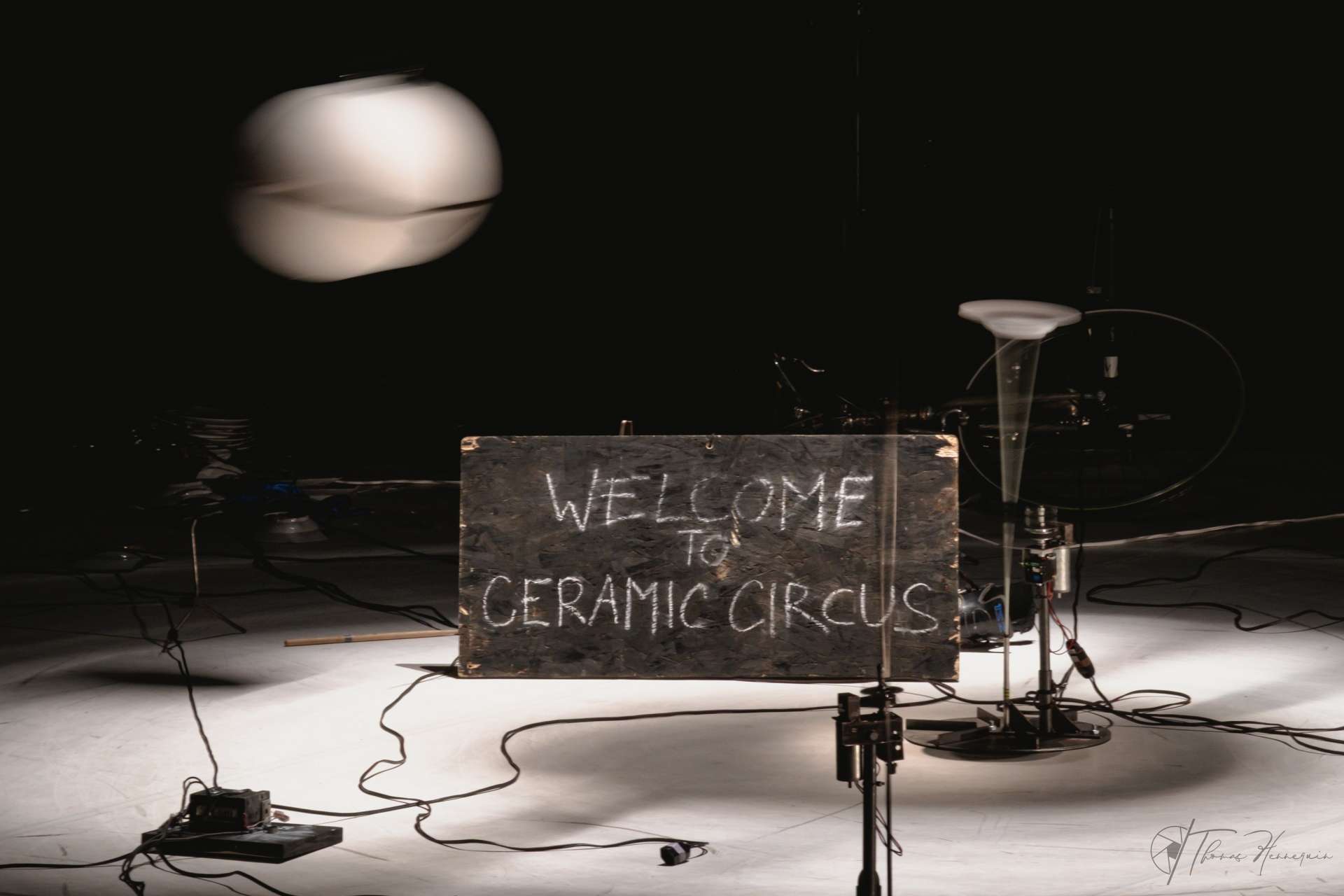 Photo du décor du spectacle. La piste est blanche, une grosse boule suspendue semble tournée et au milieu un panneau noir écrit à la craie indique : Welcome to Ceramic Circus. 