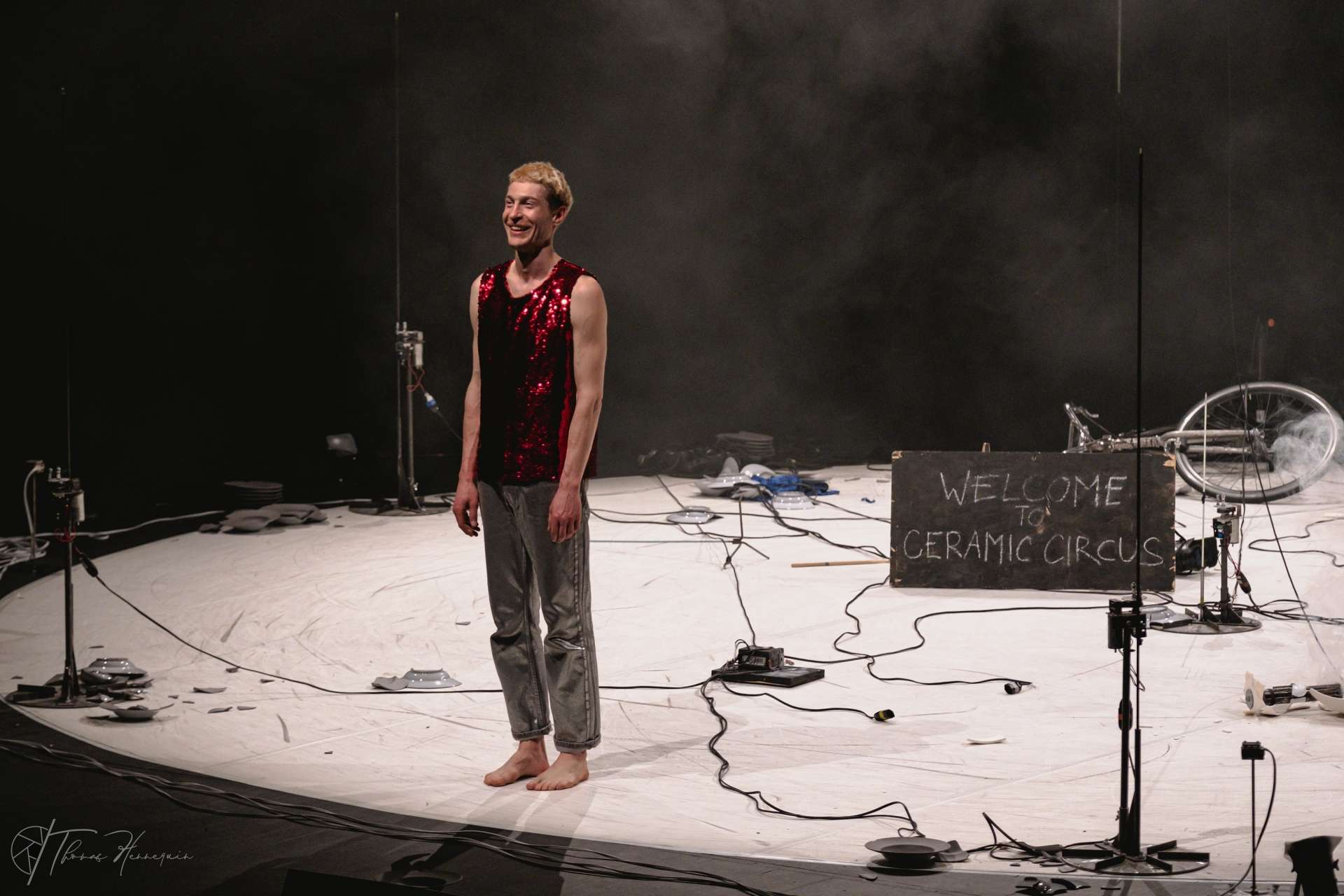 Salut de l'artiste circassien Julian Vogel. Il est vêtu d'un débardeur rouge à sequins et d'un pantalon lamé. 