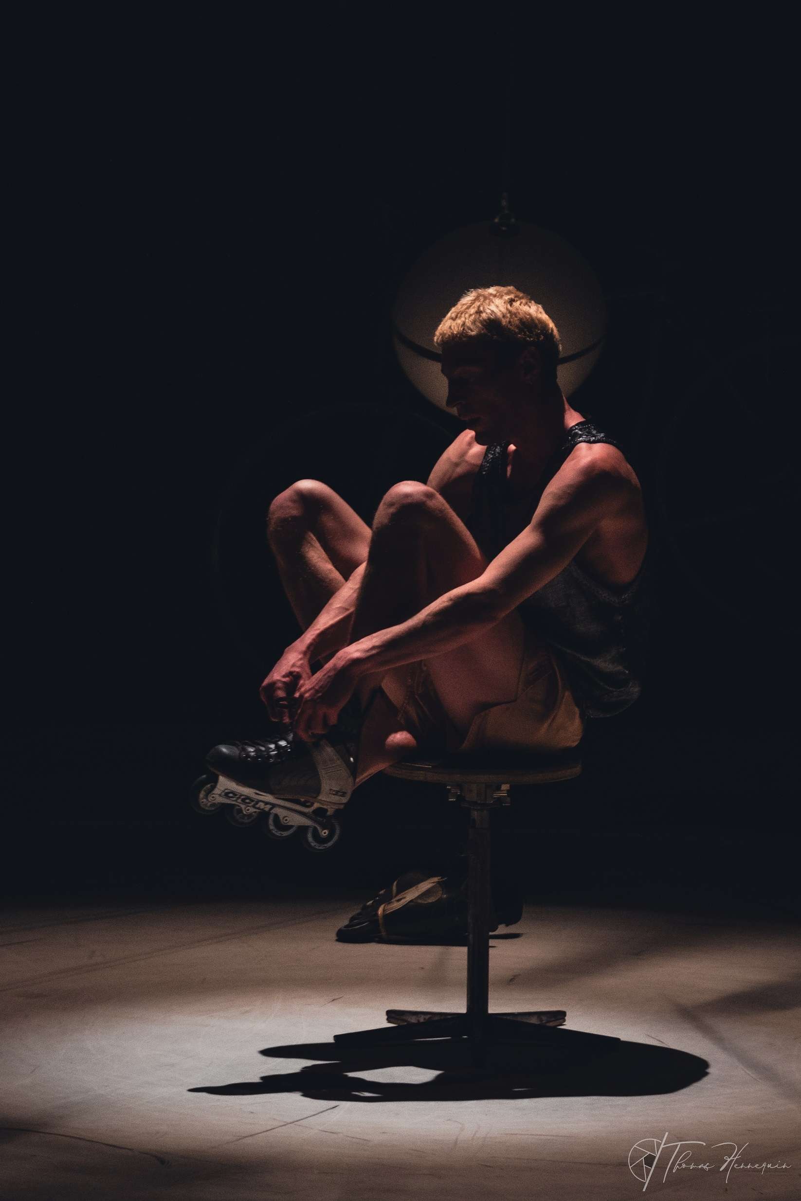 Dans l'obscurité, assis sur un siège, l'artiste circassien Julian Vogel attache ses rollers. 