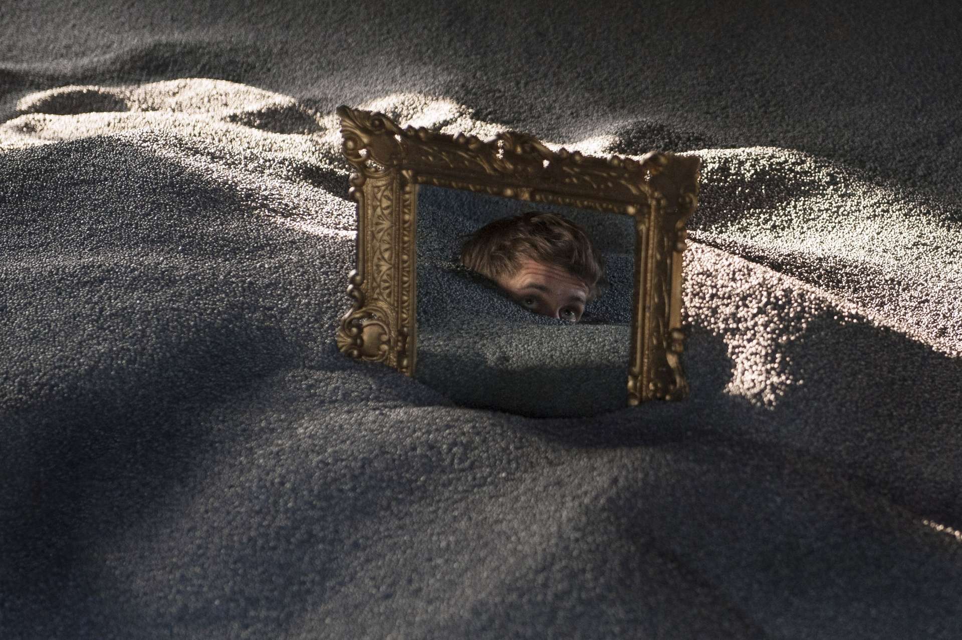 Dans le sable, un miroir est enfoncé, avec le visage d'un homme dans celui-ci.