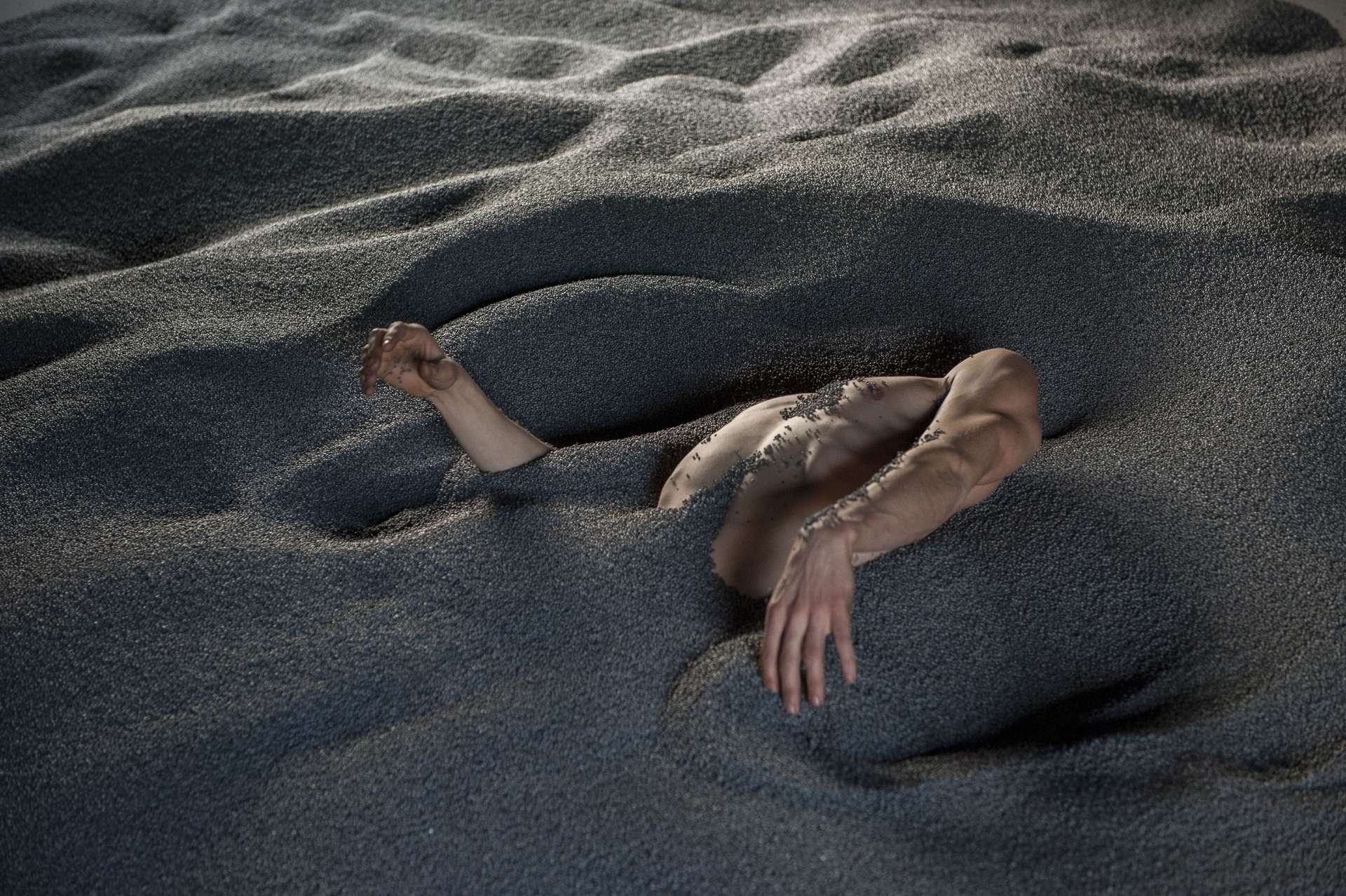 Un homme est allongé dans le sable, sa tête et ses jambes enfoncées, ses bras sont en mouvement. 