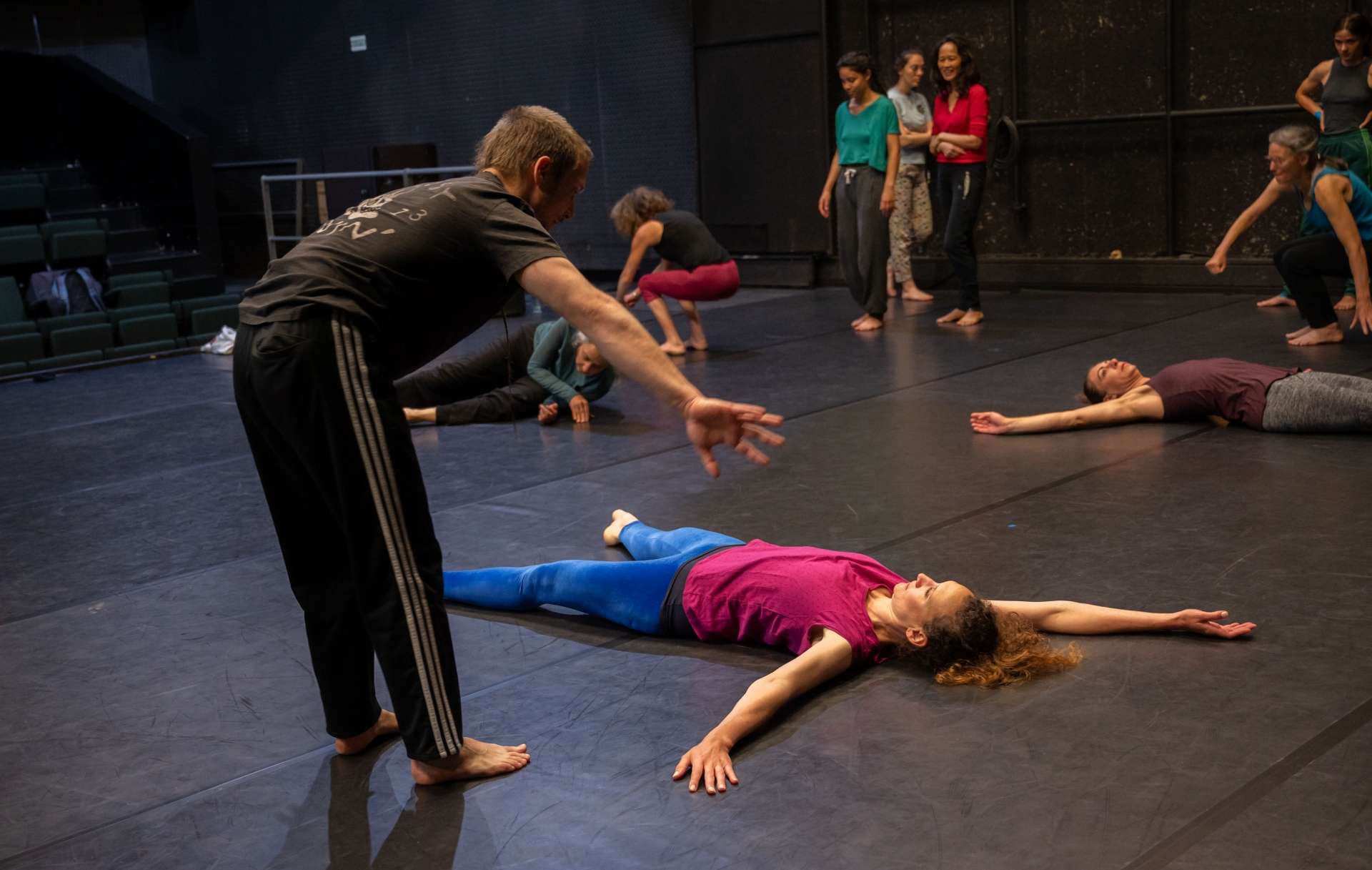 Photo de l'atelier de danse acrobatique, Clotaire au dessus des participant·es donnent des consignes, eux sont allongé·es sur le sol, les bras et jambes écartés.