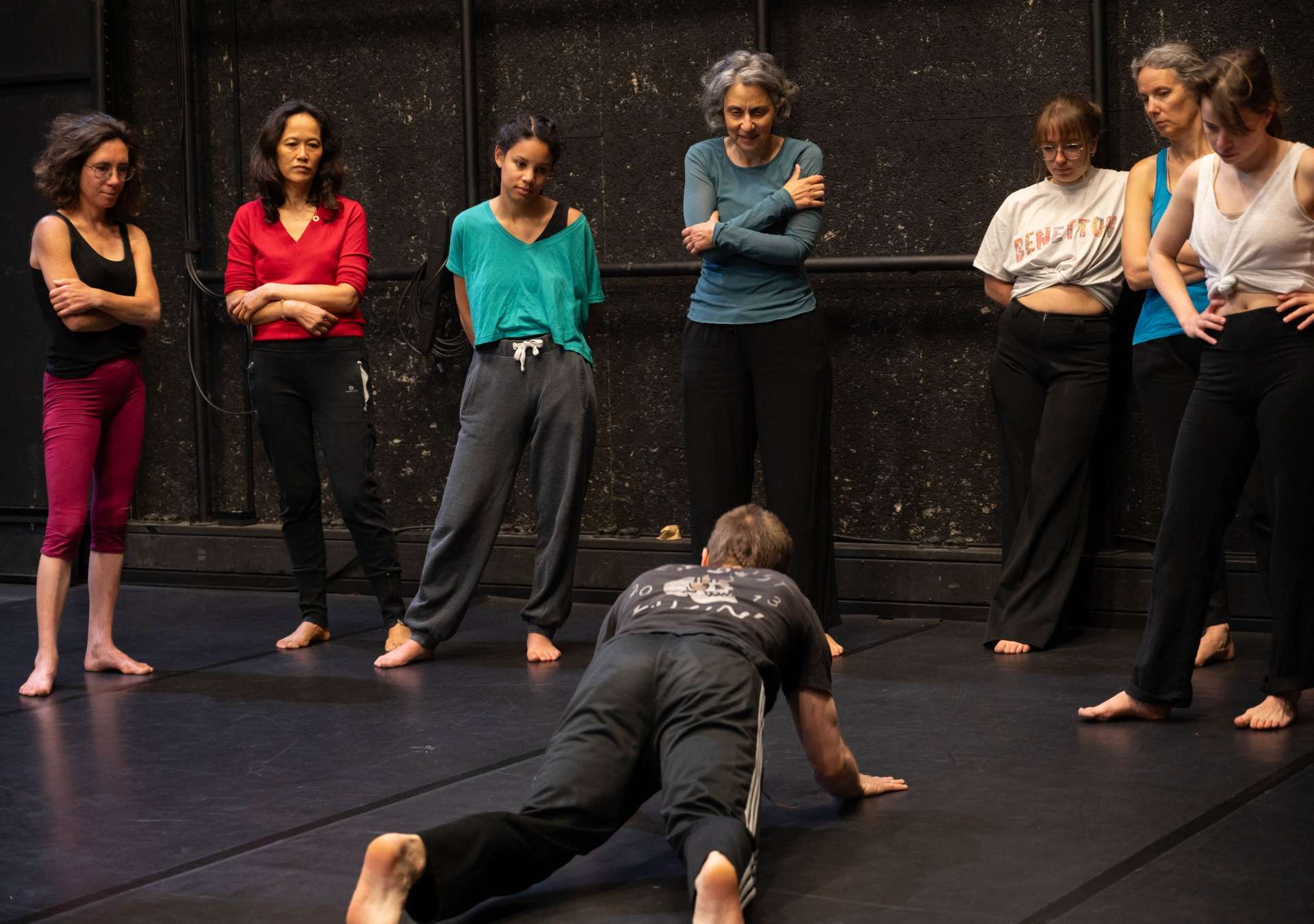 Photo de l'atelier de danse acrobatique, Clotaire en premier plan est en position gainage devant les participant·es qui regardent en arrière plan et écoutent les instructions.