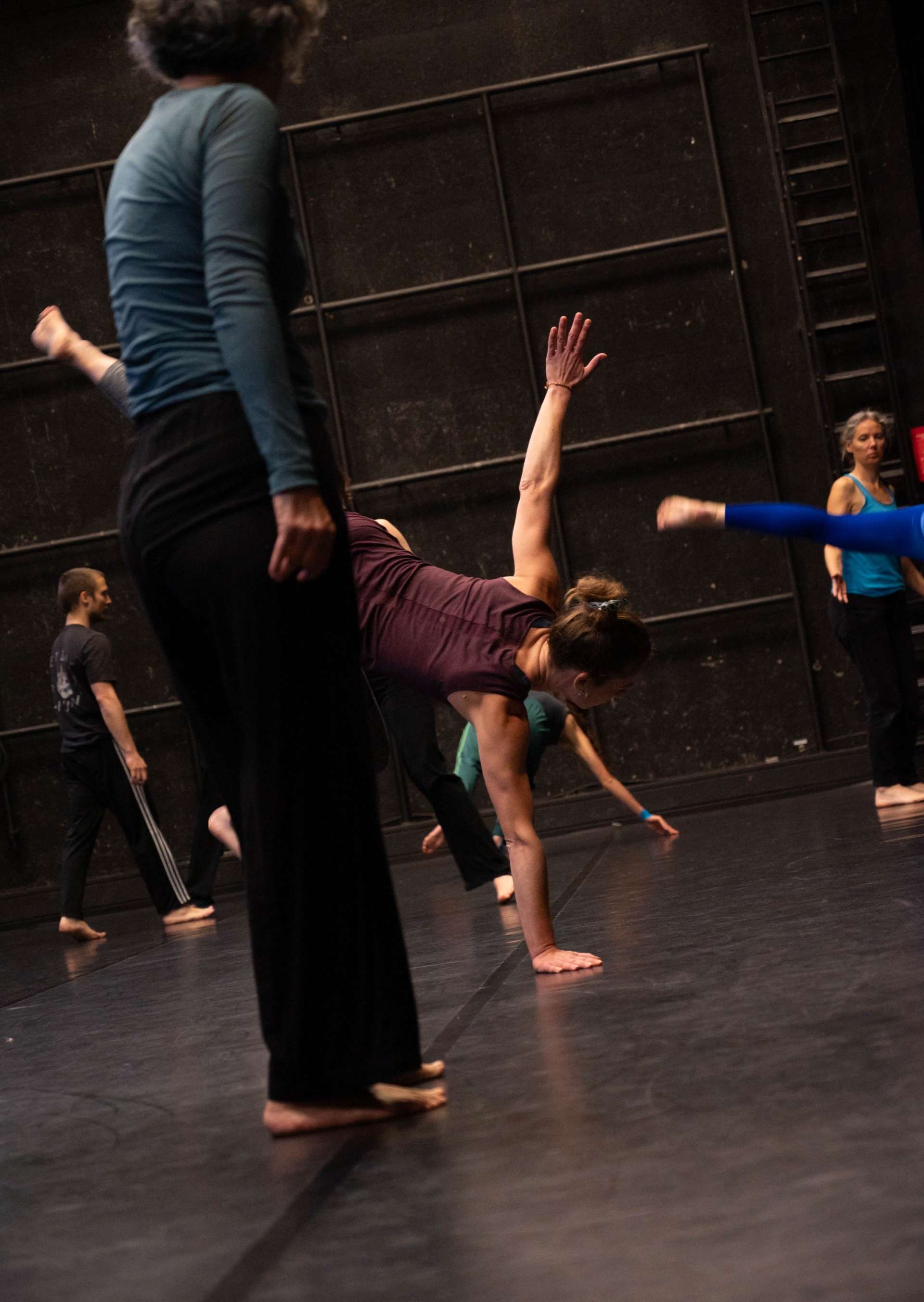 Photo de l'atelier de danse acrobatique, en premier plan une participante debout qui regarde une autre participante qui tente une figue au sol. 