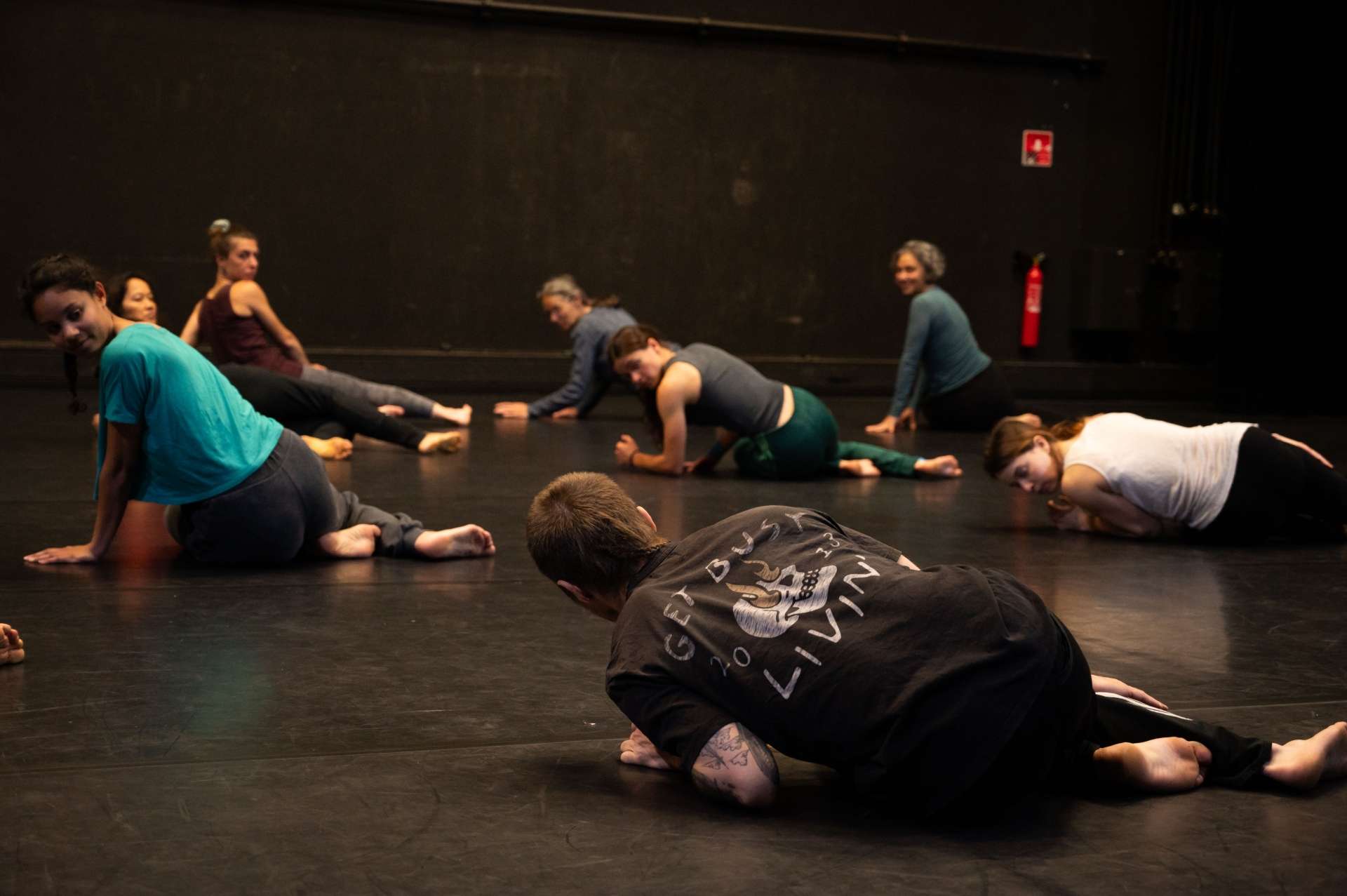 Photo de l'atelier de danse acrobatique, Clotaire en premier plan allongé sur le sol, montre l'exemple. Les participant.es suivent ses mouvements. 