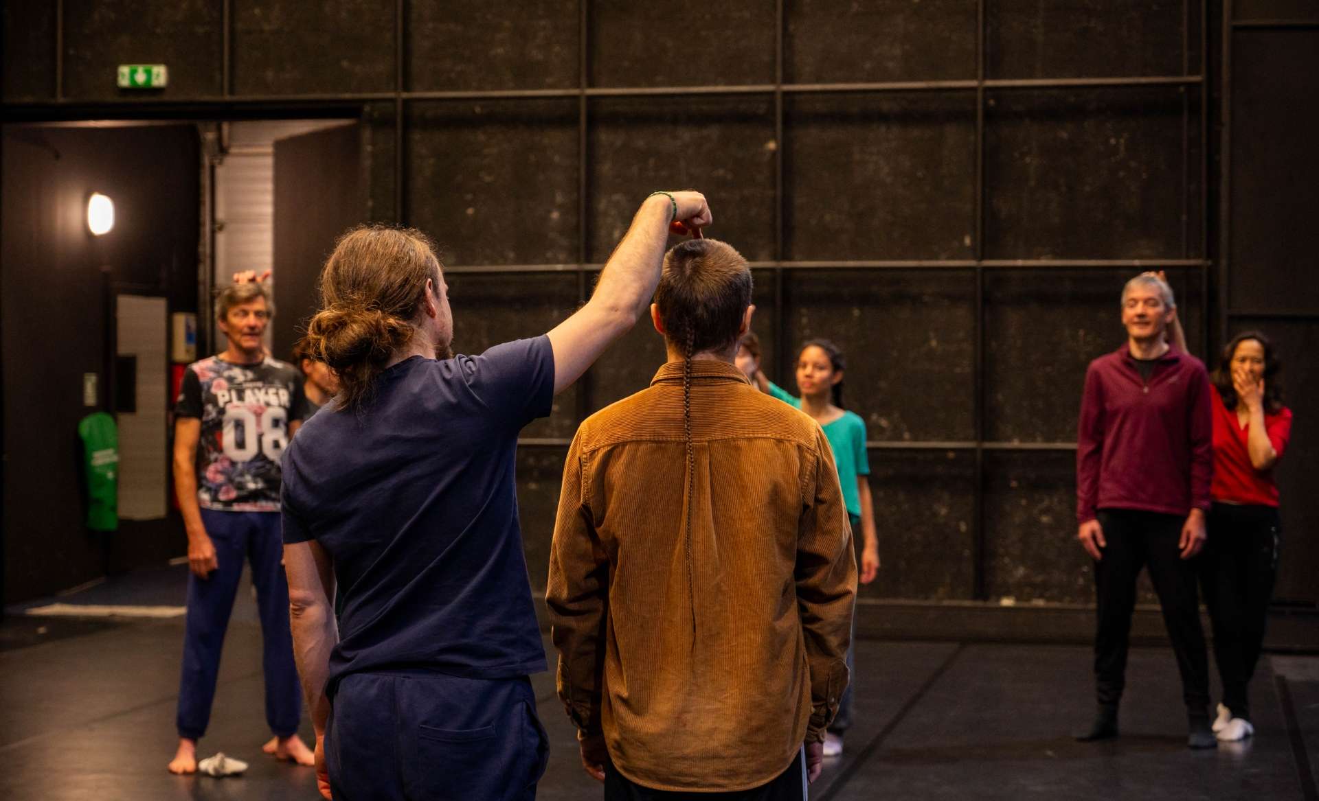 Photo de l'atelier de danse acrobatique, focus sur un duo, le dos tourné. L'un derrière le doigt sur le haut de la tête de l'autre personne qui se tient devant afin de trouver le point d'équilibre du corps.